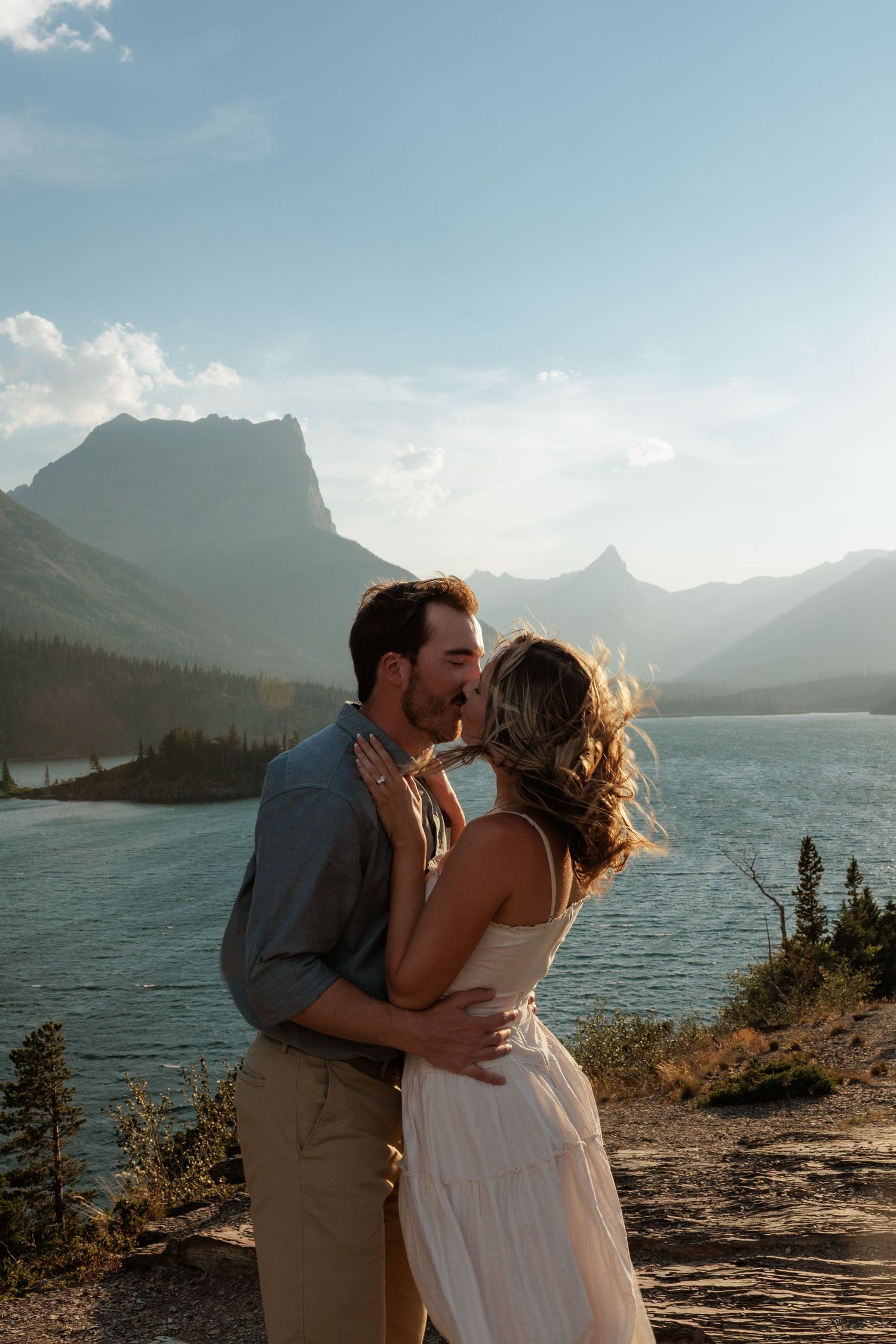 Couple sharing a romantic kiss with a stunning backdrop of Saint Mary Lake on Sun Point in Glacier National Park during golden hour.