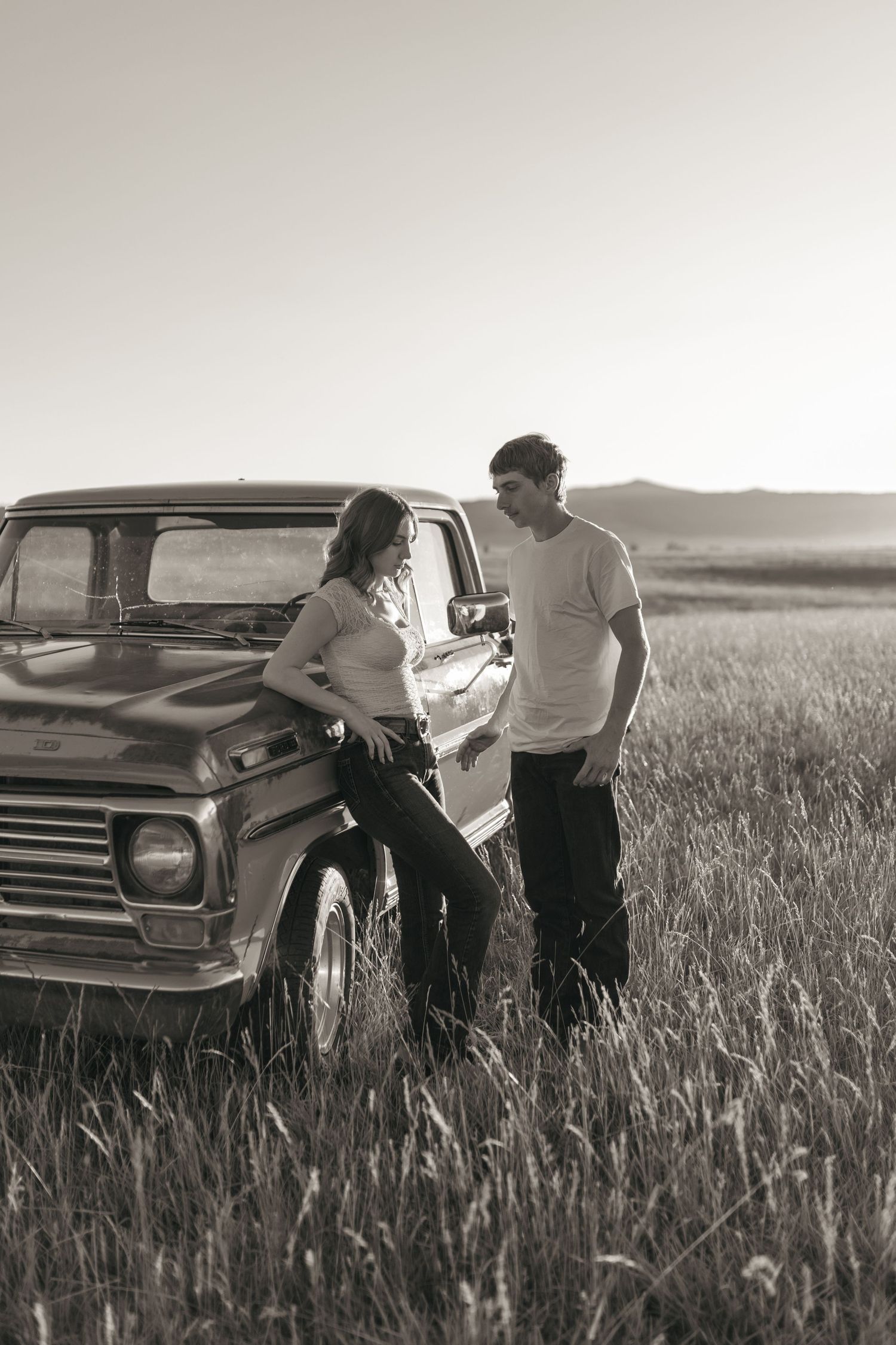 A vintage pickup truck parked in a grassy field is being examined by two people in a black and white photo.