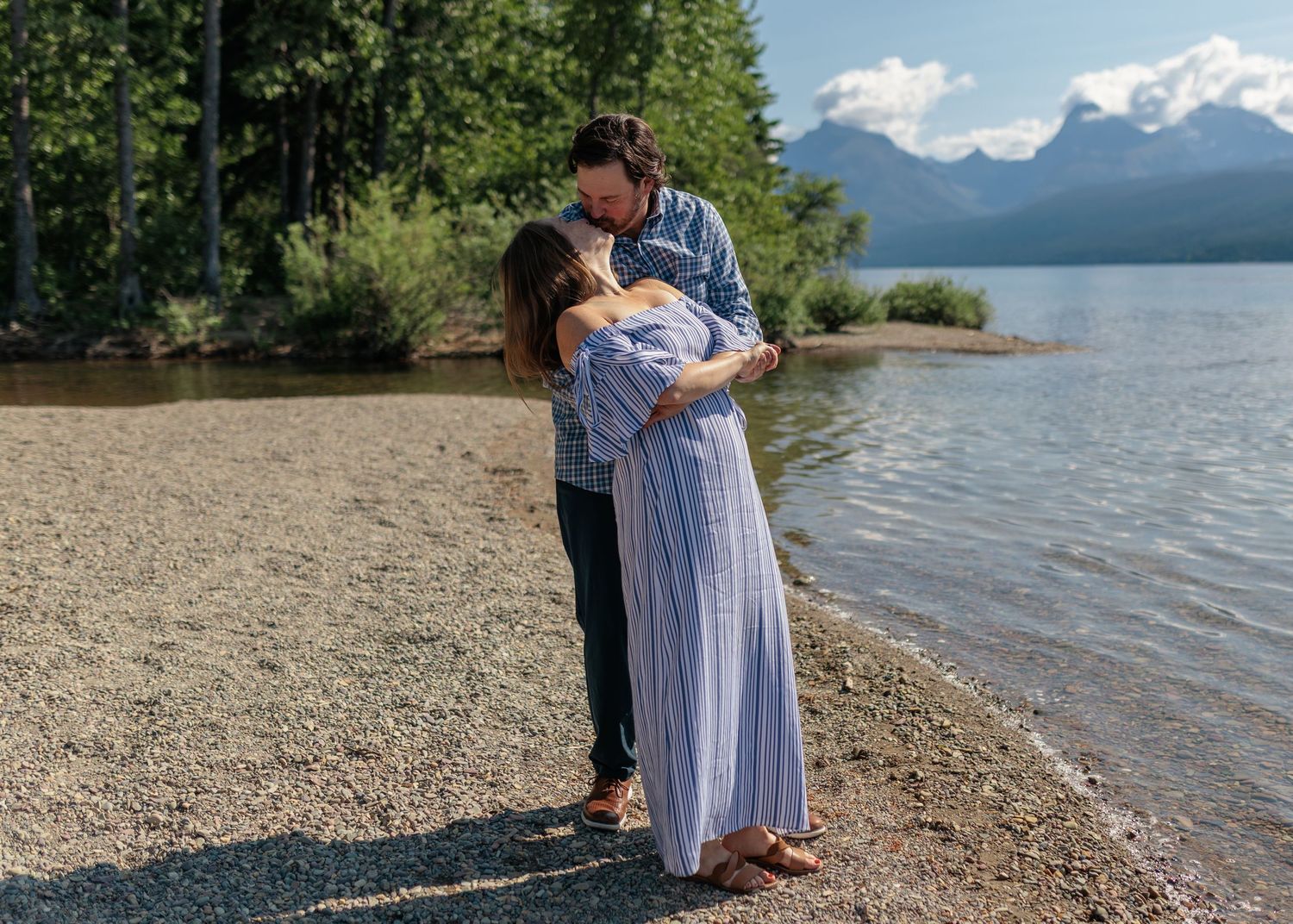 A couple enjoys a romantic moment at the shoreline of a mountain lake on a sunny summer afternoon.