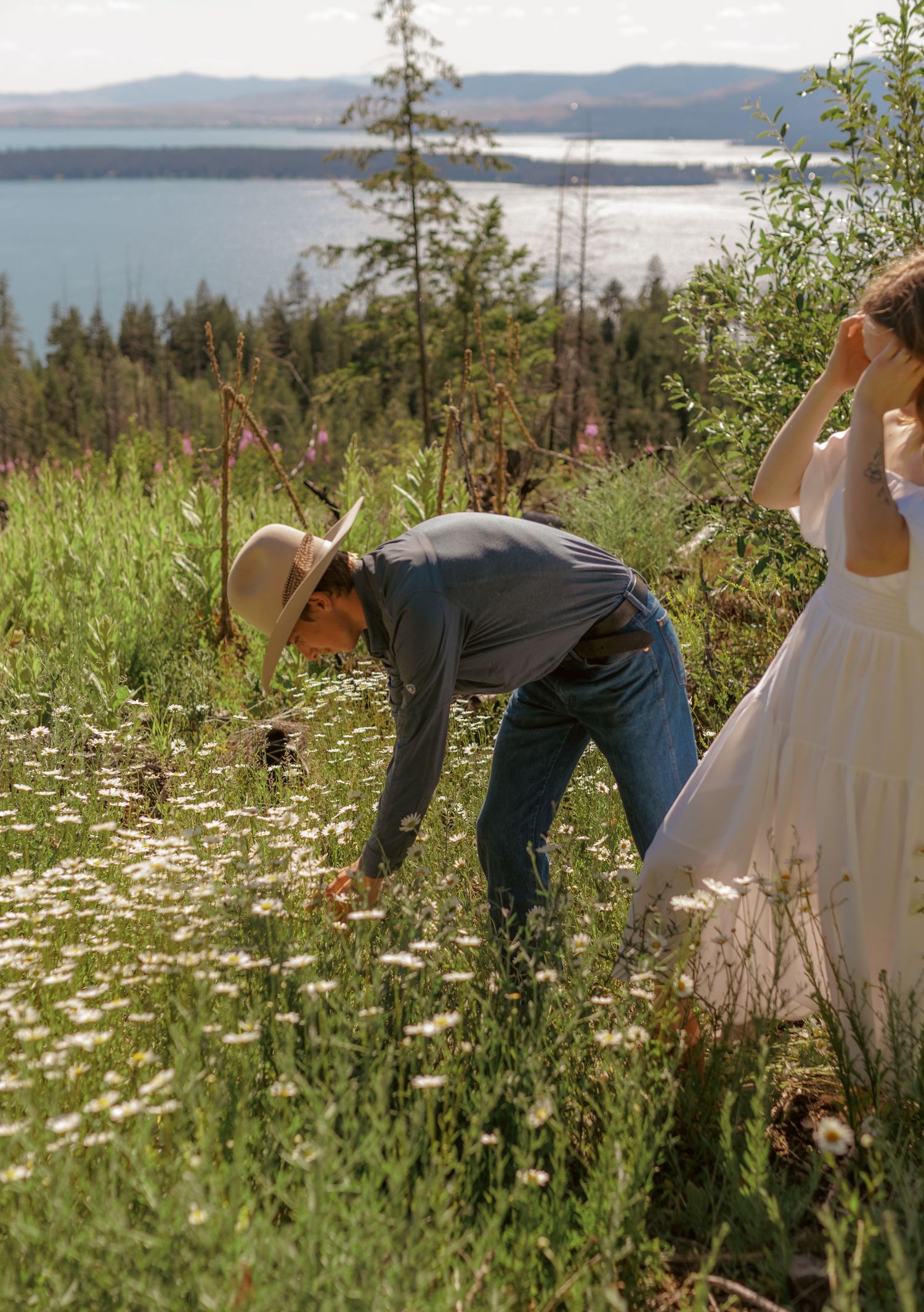 Two people dance playfully through a mountain meadow filled with white daisies.