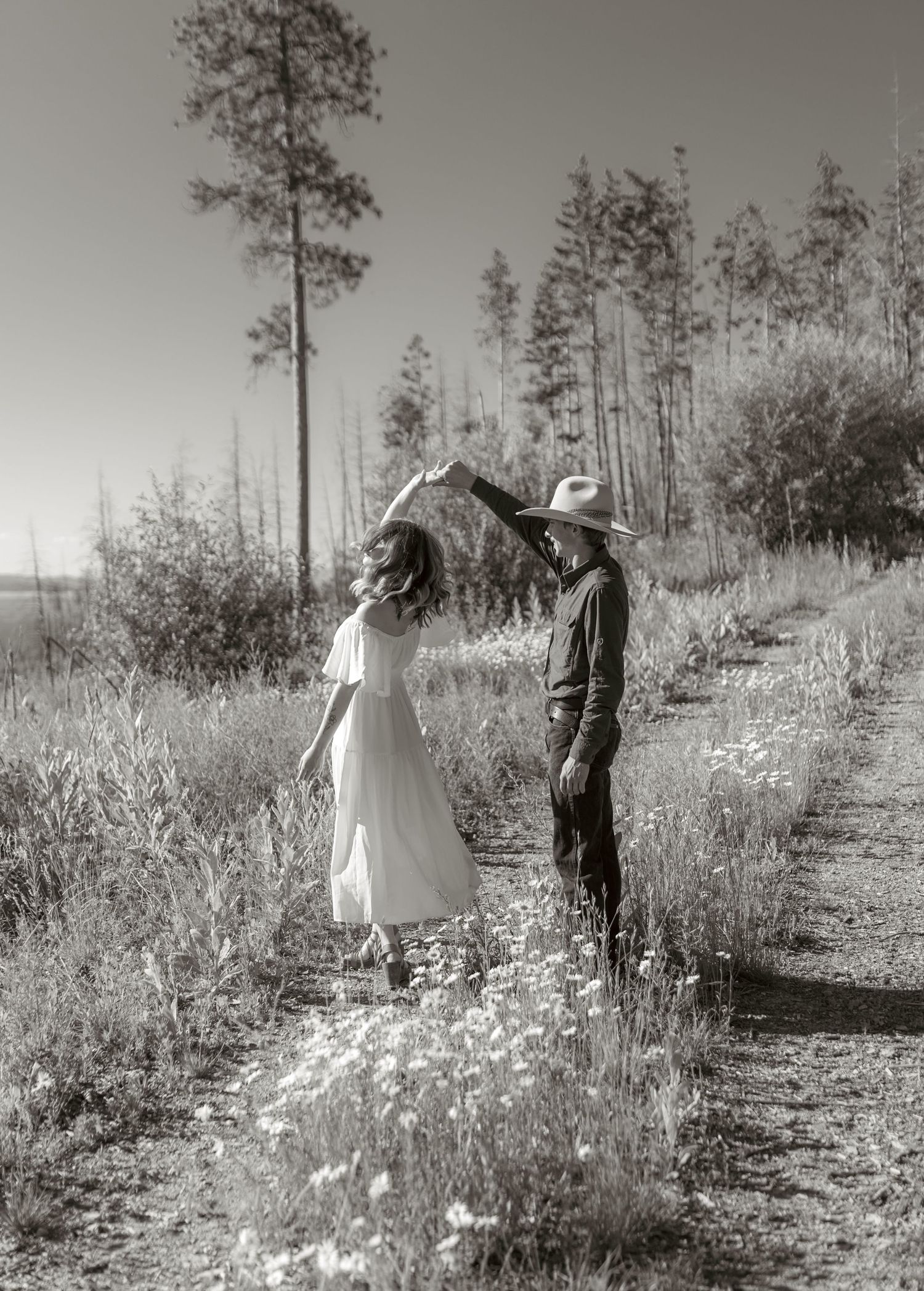 A black and white photo captures a romantic moment between two people in a meadow.