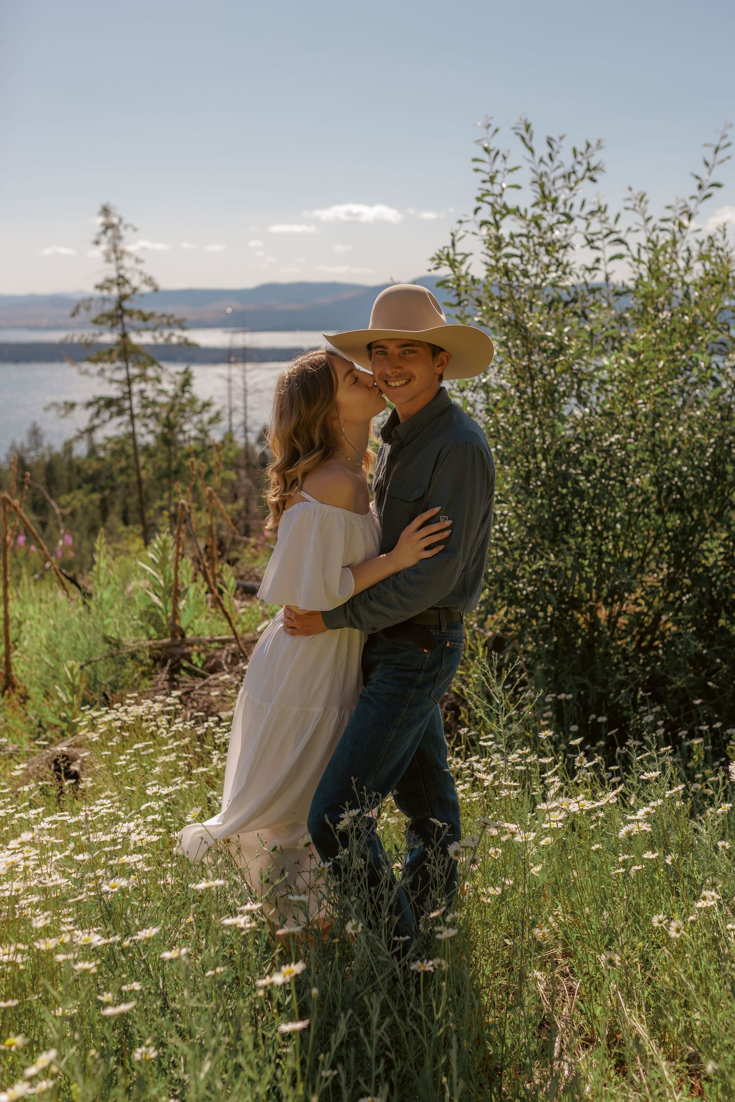Intimate moment between couple in a sunny wildflower meadow with lake views.