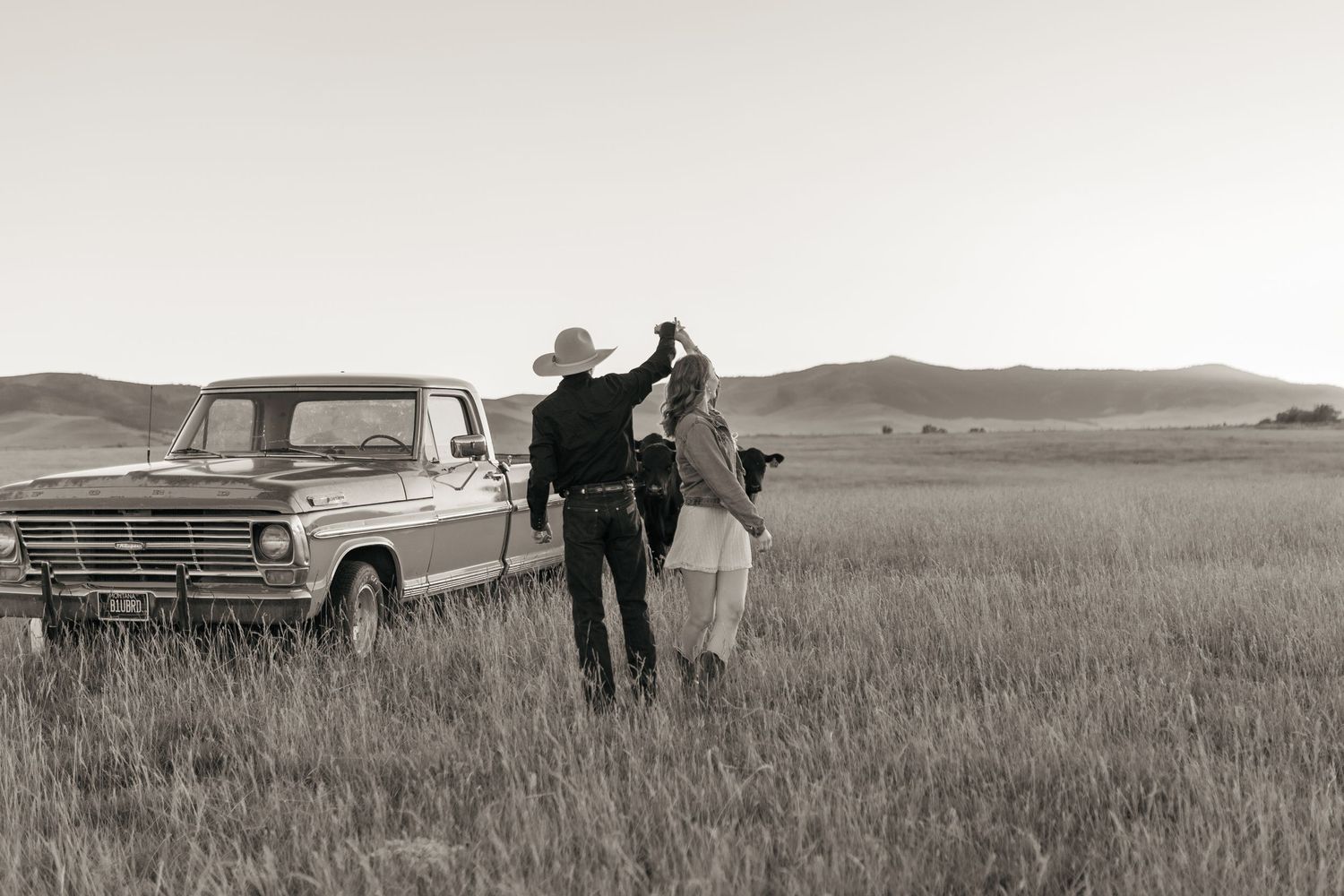 A couple shares a romantic moment beside their vintage pickup truck in a vast grassy field.