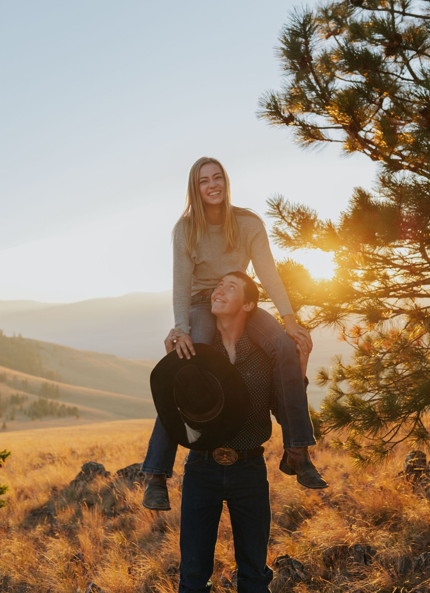 Playful couple shares joyful moments against mountain scenery during golden hour.