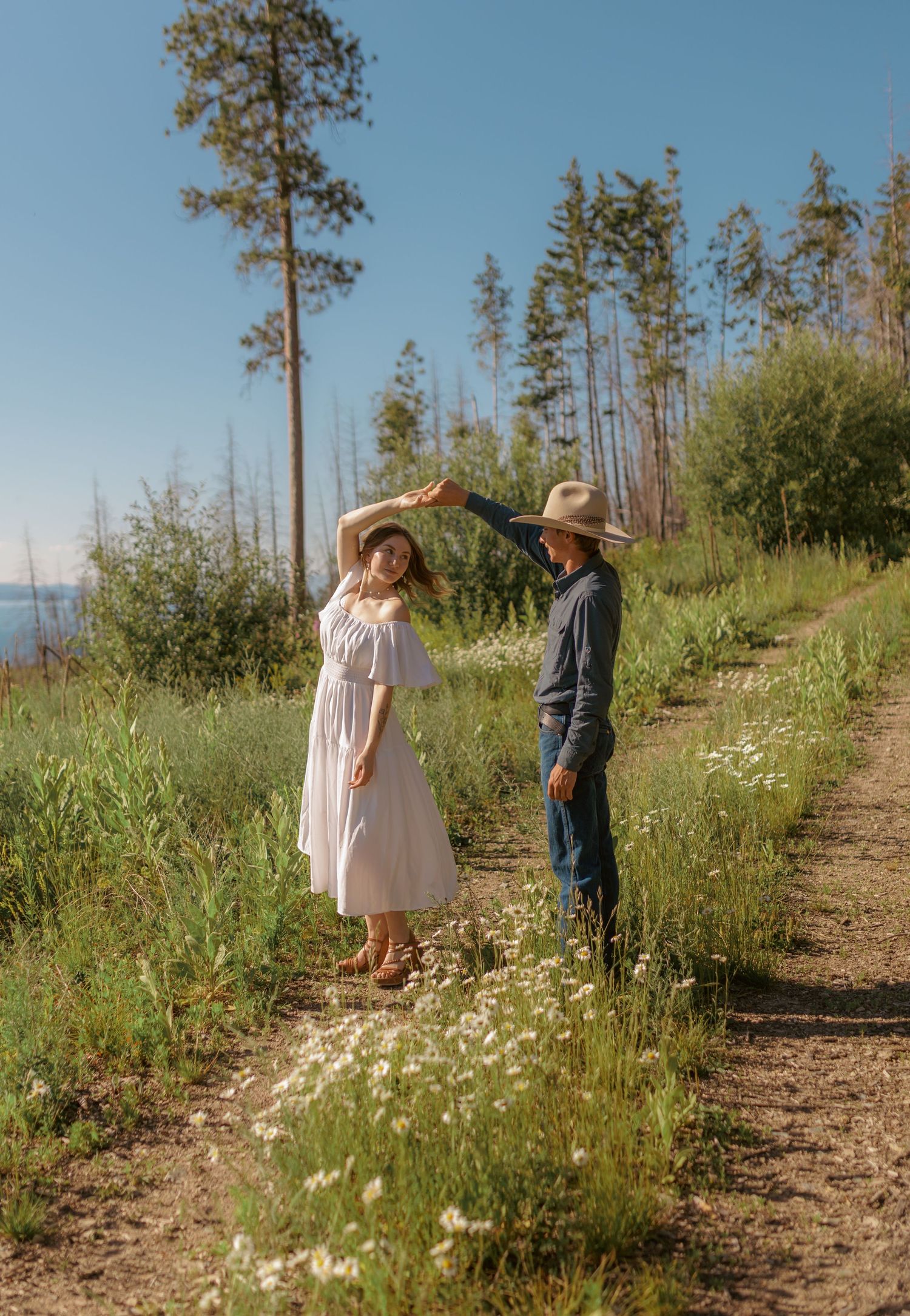 Two people share a tender moment while walking through a sunny mountain meadow.