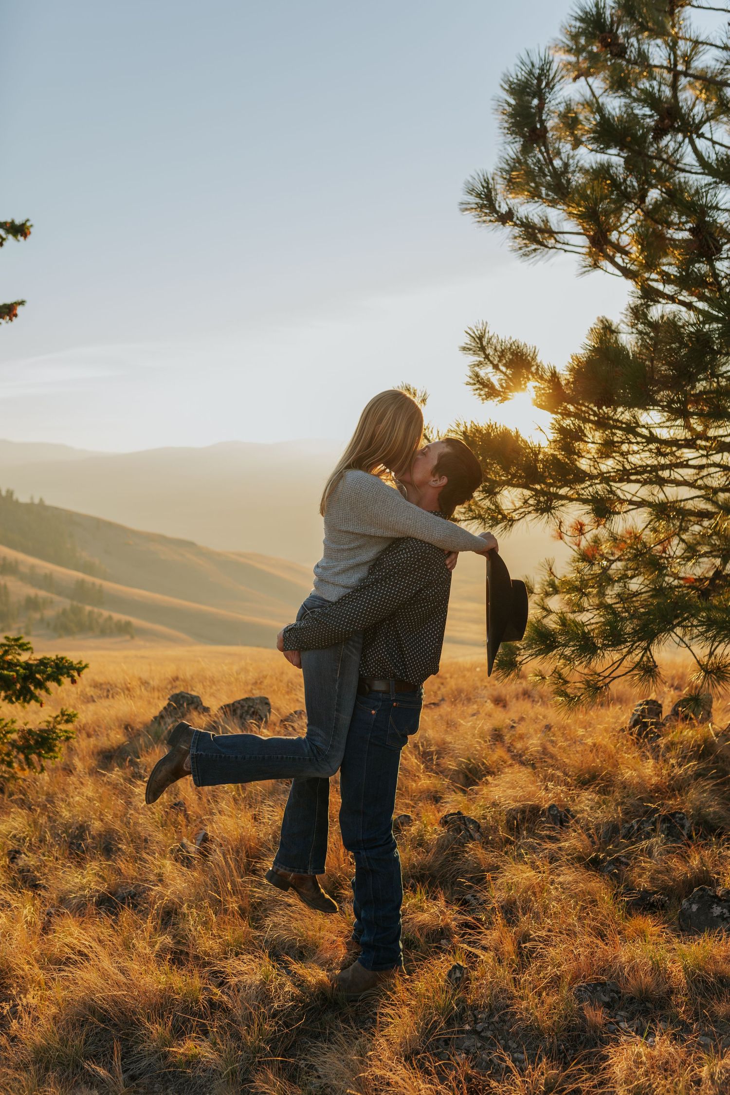 A couple shares a romantic moment in golden sunset light on a hilltop.