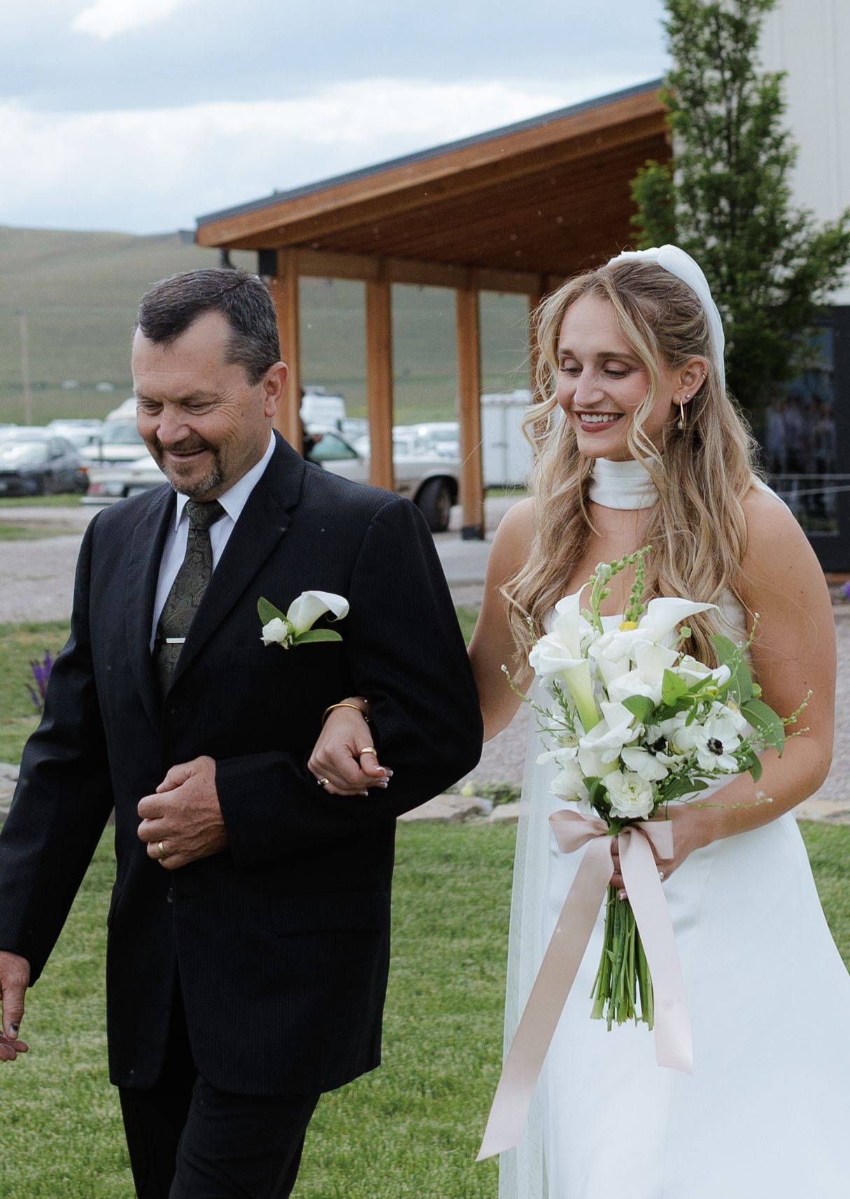 Bride in white gown holding bouquet walks with her dad at Montana wedding ceremony with views of the mission mountains