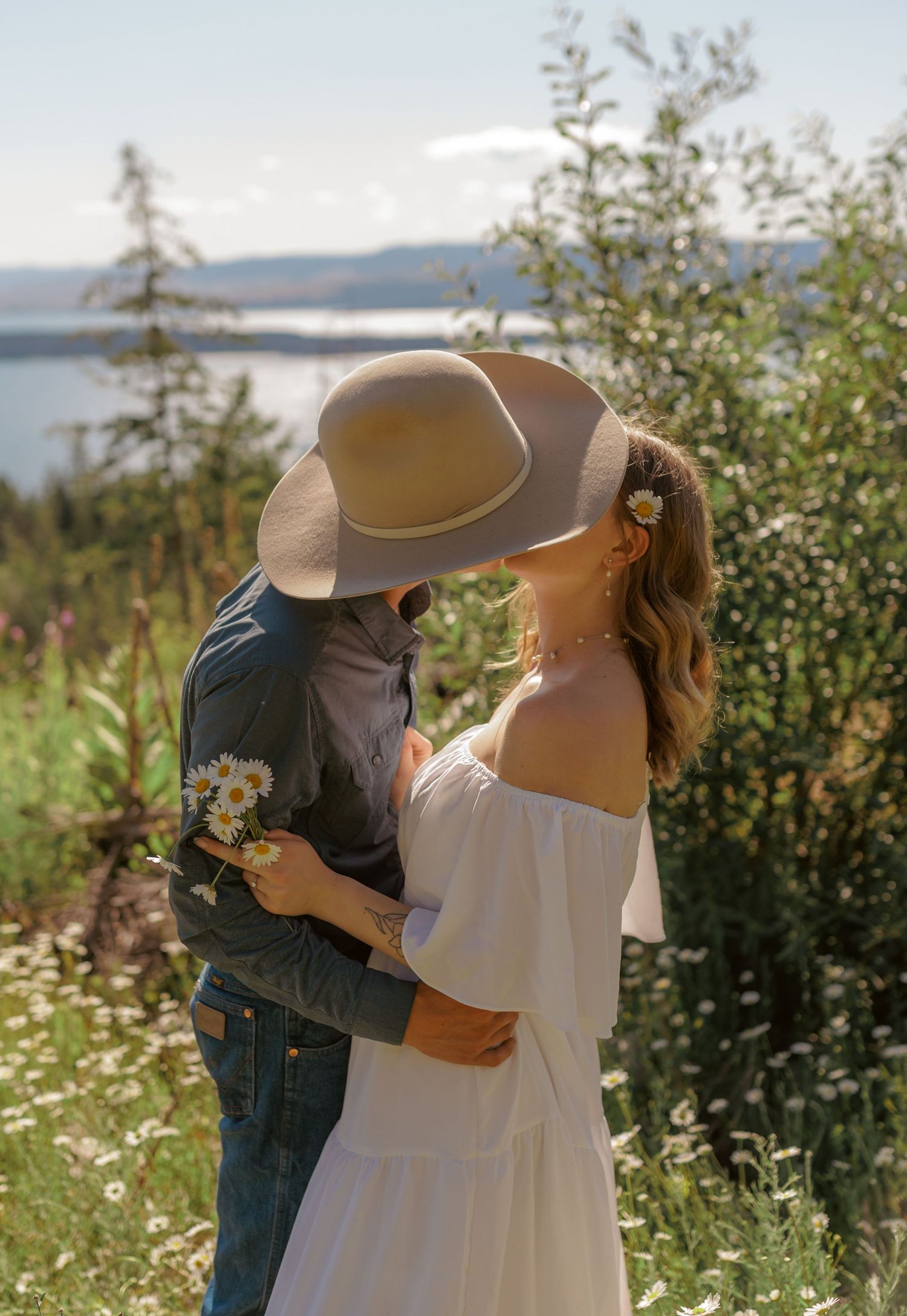 An intimate embrace between two people in white and denim against a natural landscape.