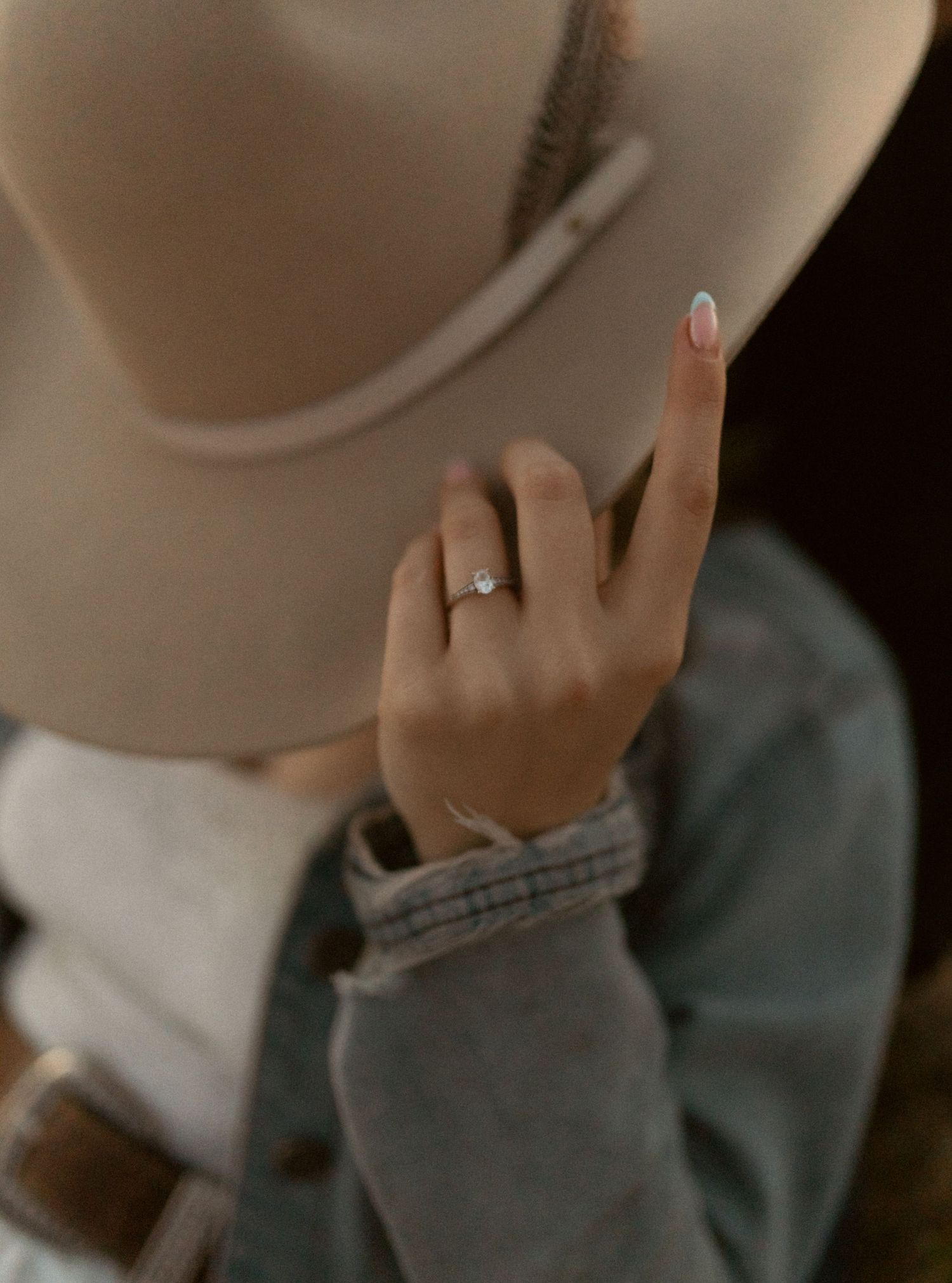 Close-up of a hand wearing an engagement ring and touching the brim of a tan cowboy hat.