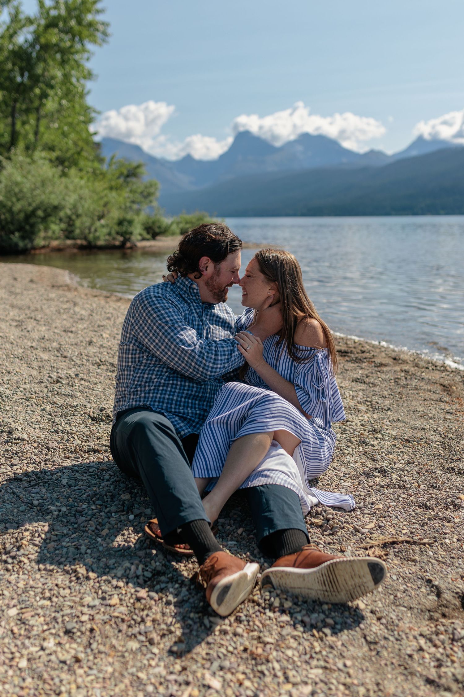 A romantic moment shared between a couple sitting on a rocky shoreline with mountain views.