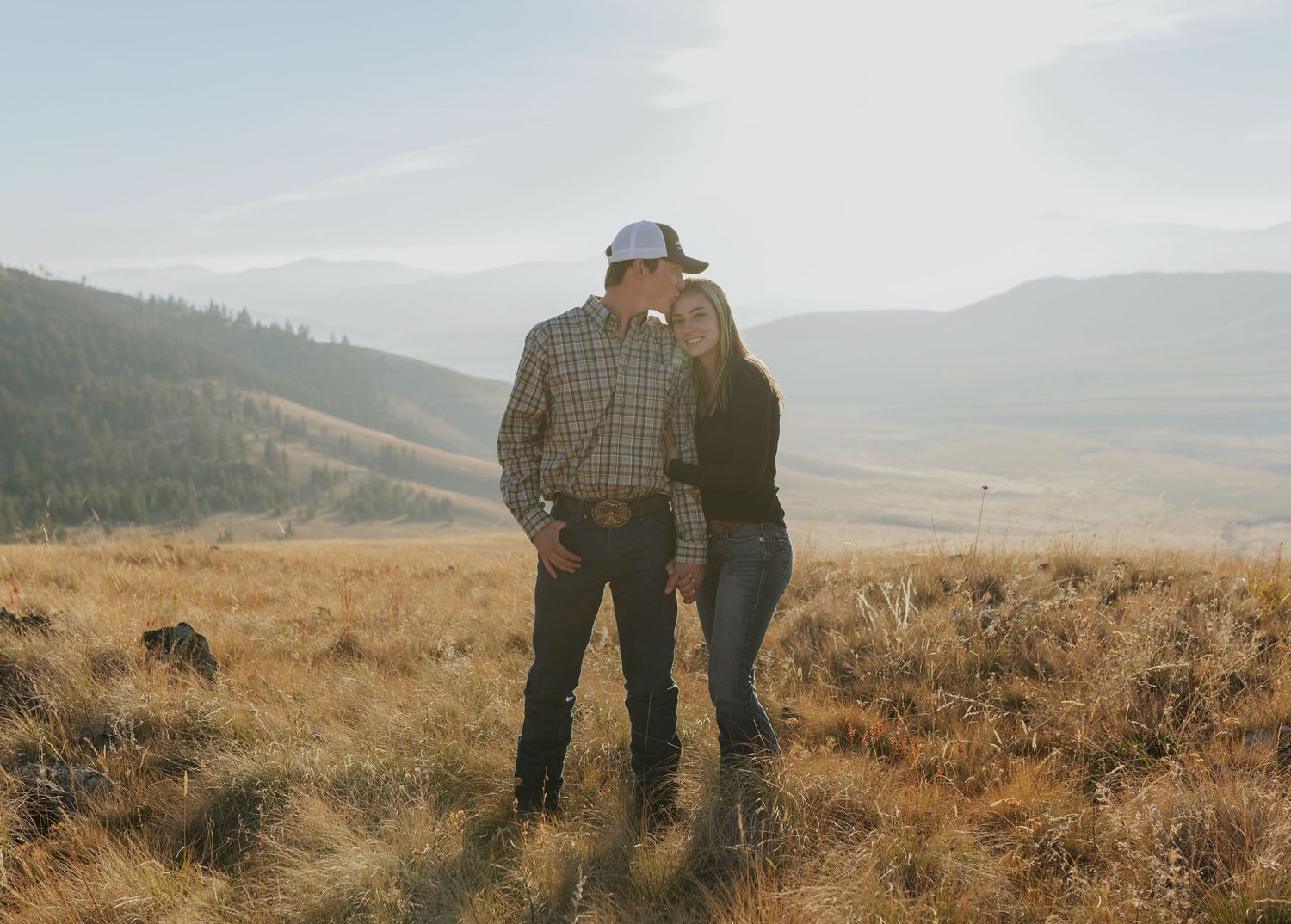 A couple stands together on a golden hillside at dusk.