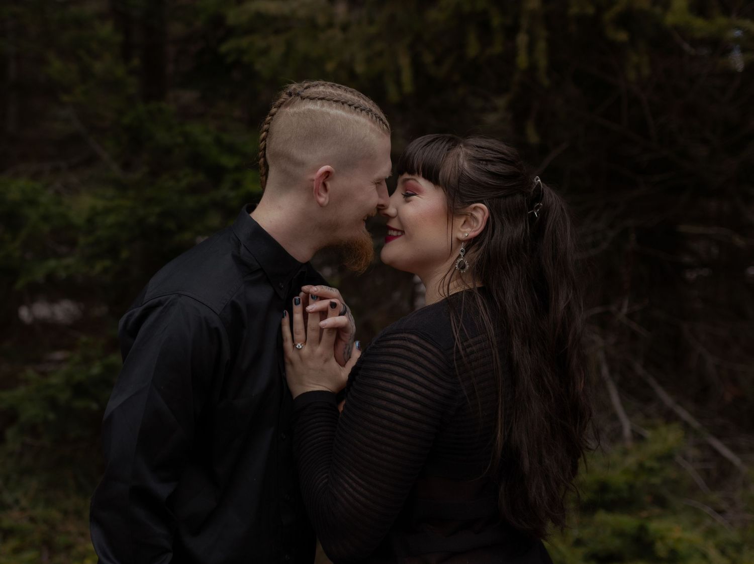 A couple shares an intimate moment together in a moody forest setting.