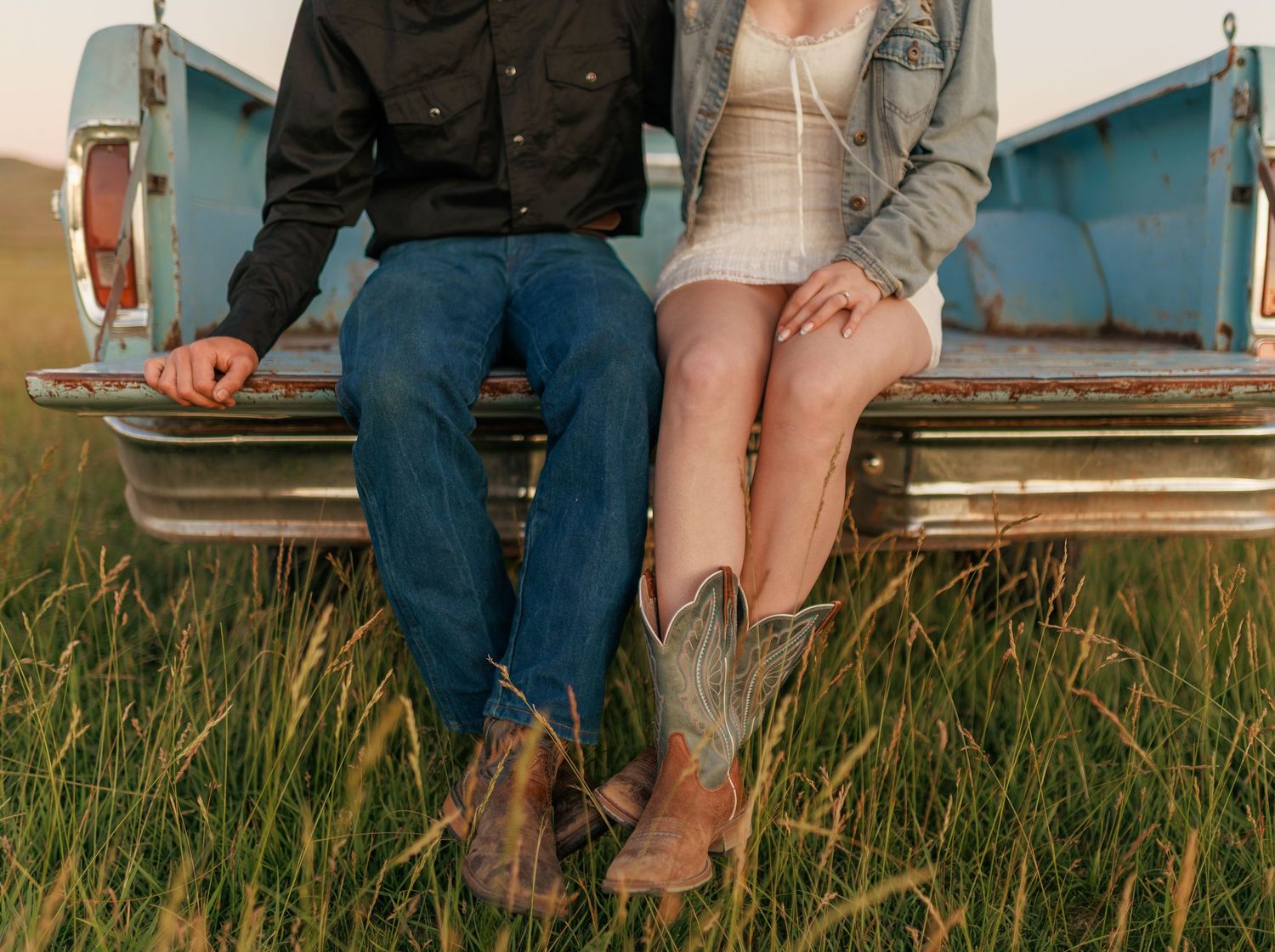 Couple sits casually on tailgate of vintage truck in tall prairie grass.