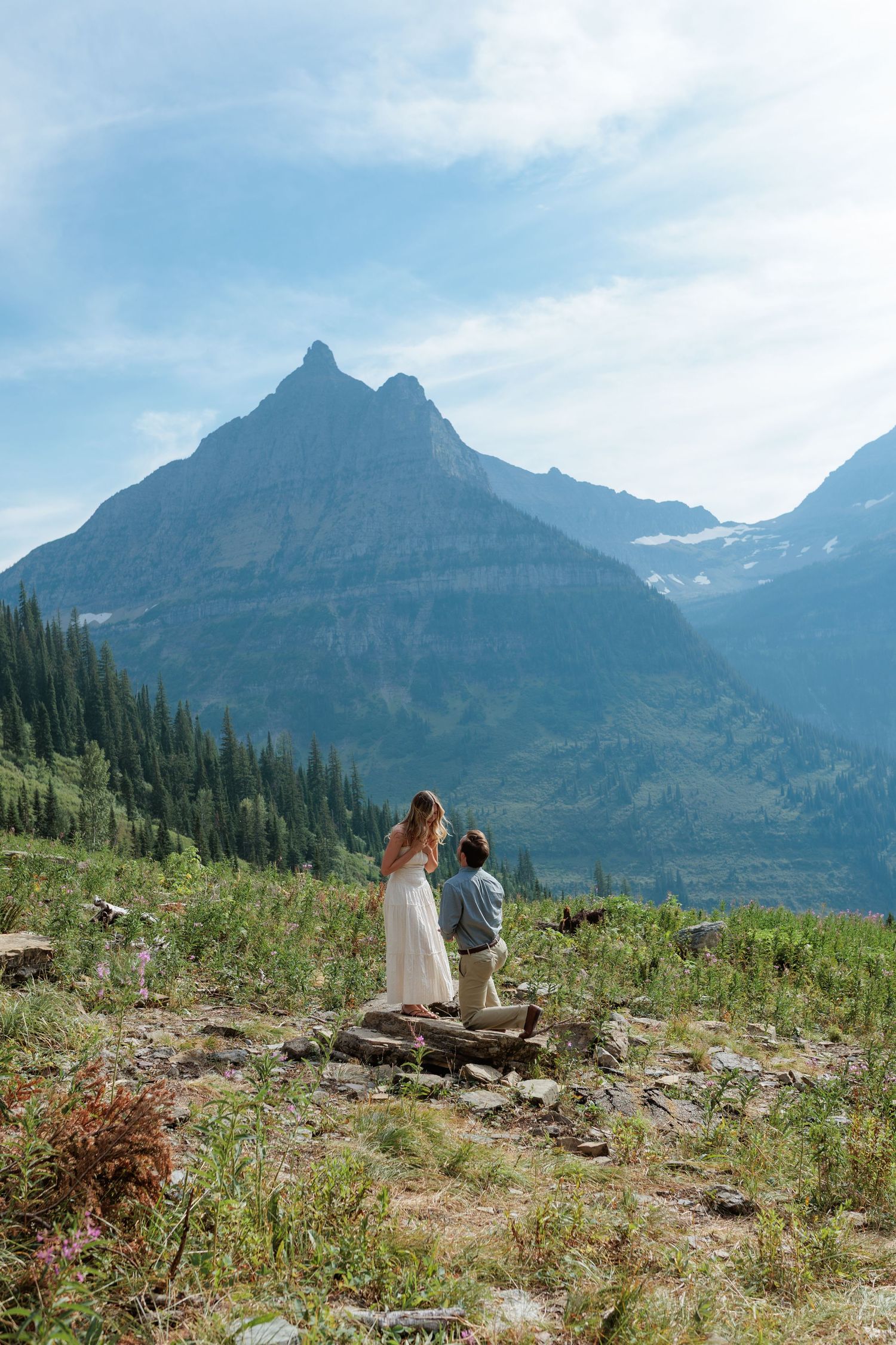 Man proposing to girlfriend in front of dramatic mountain peak backdrop at Big Bend in Glacier National Park