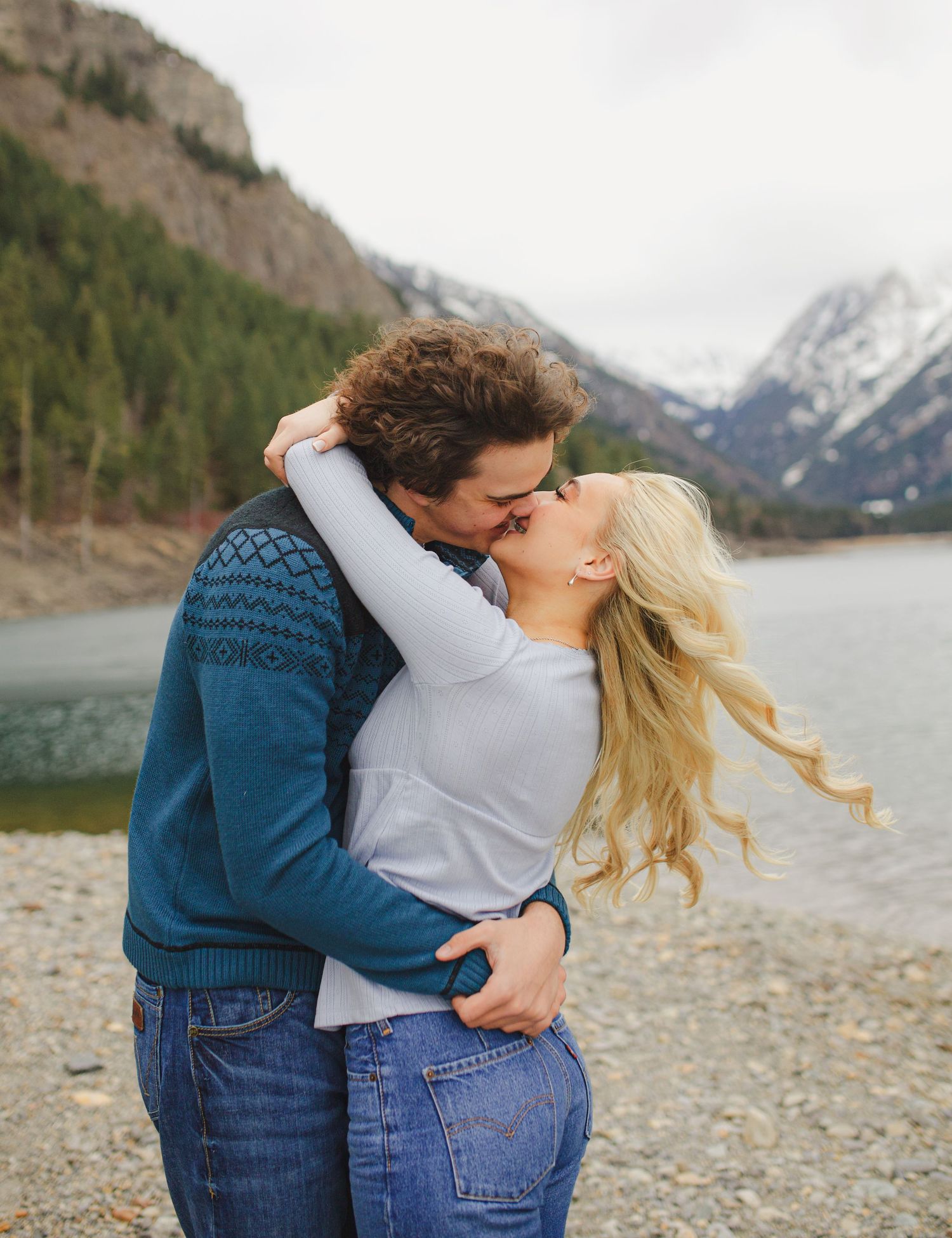 Romantic embrace by a mountain lake with snow-capped peaks in the distance.