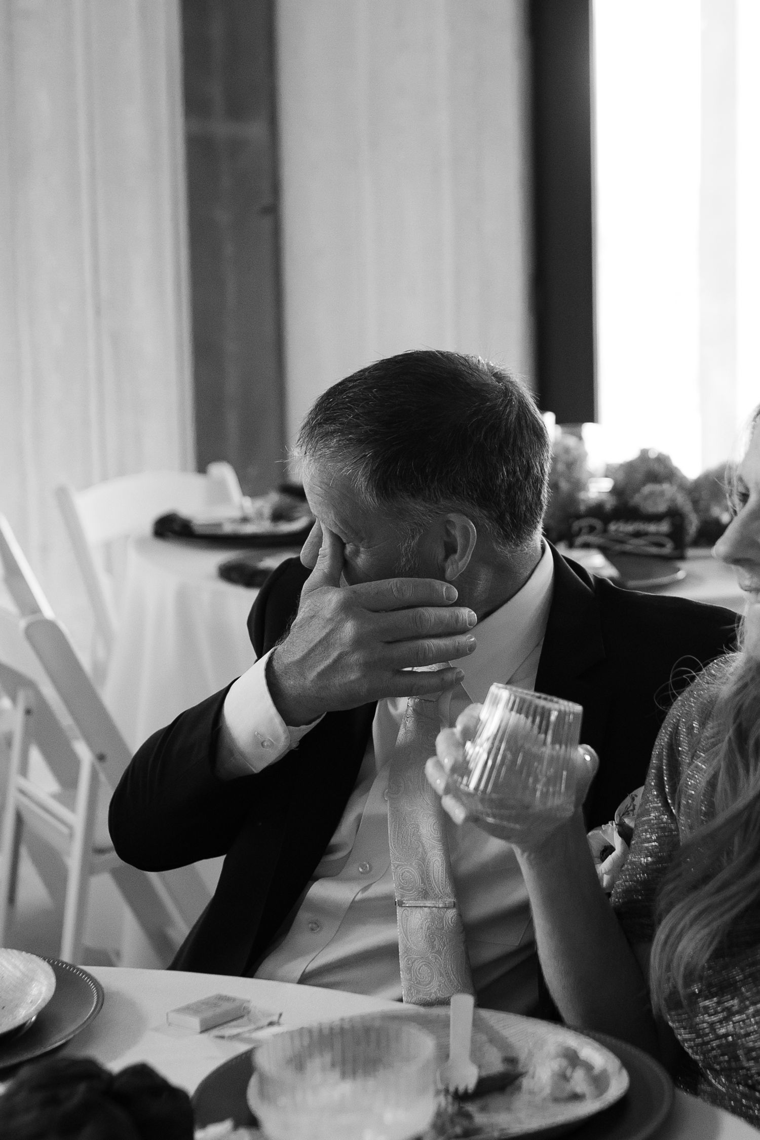 Black and white photo of the father of the groom wiping away a tear listening to a wedding speech at Montana wedding