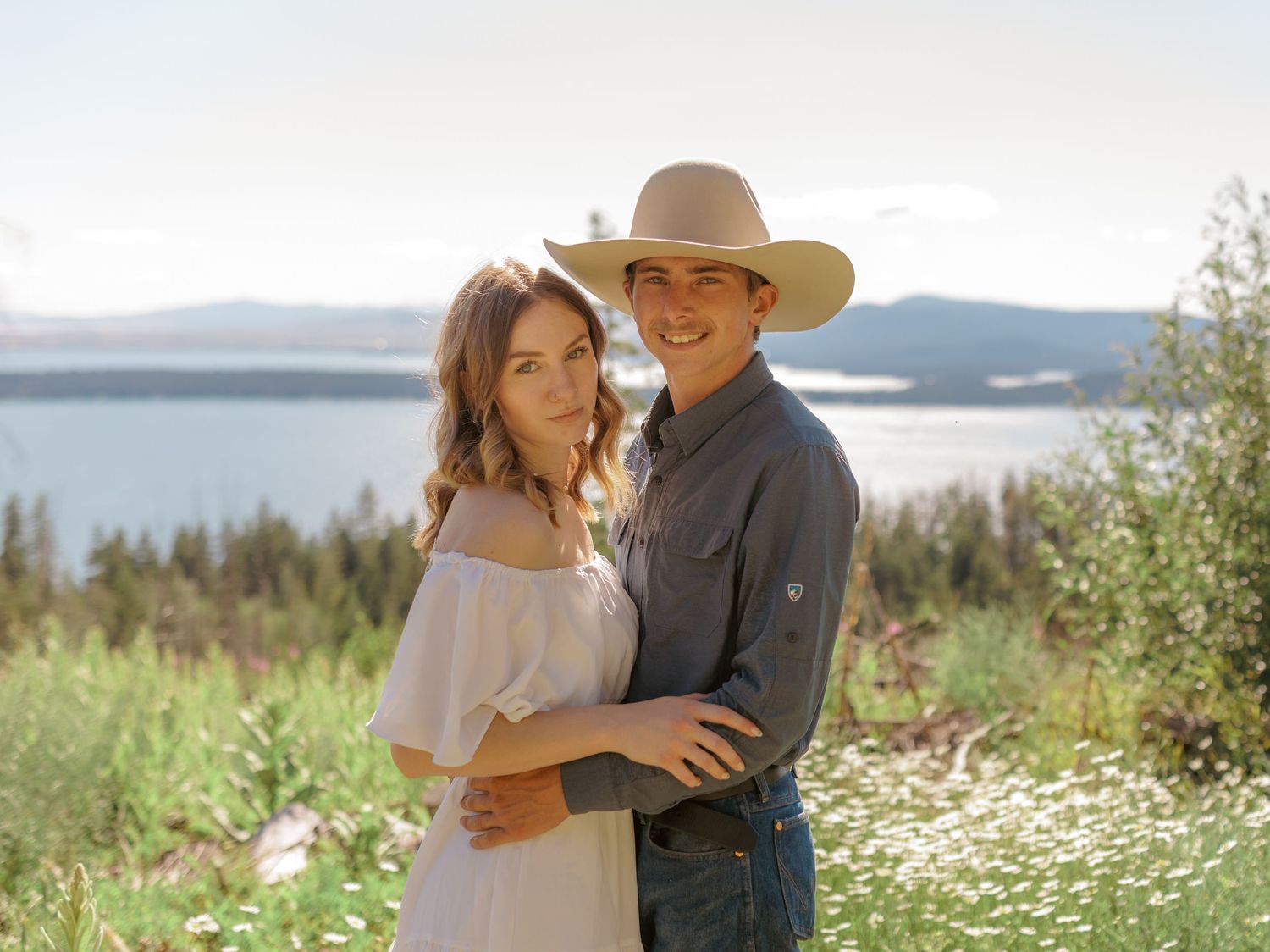 A couple shares sweet moments in a serene mountain meadow landscape.