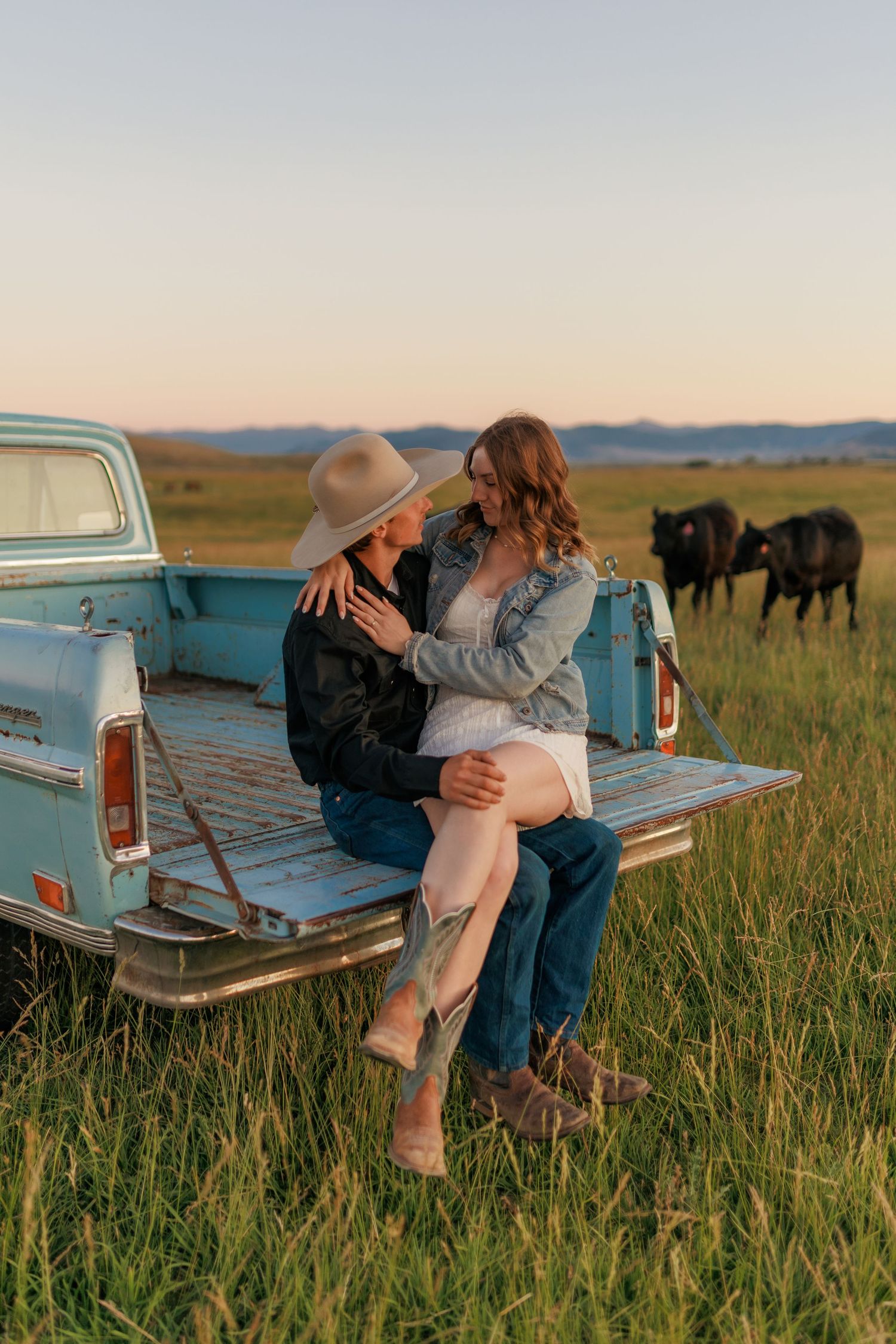 Romantic couple sitting on vintage truck bed in prairie field at sunset.