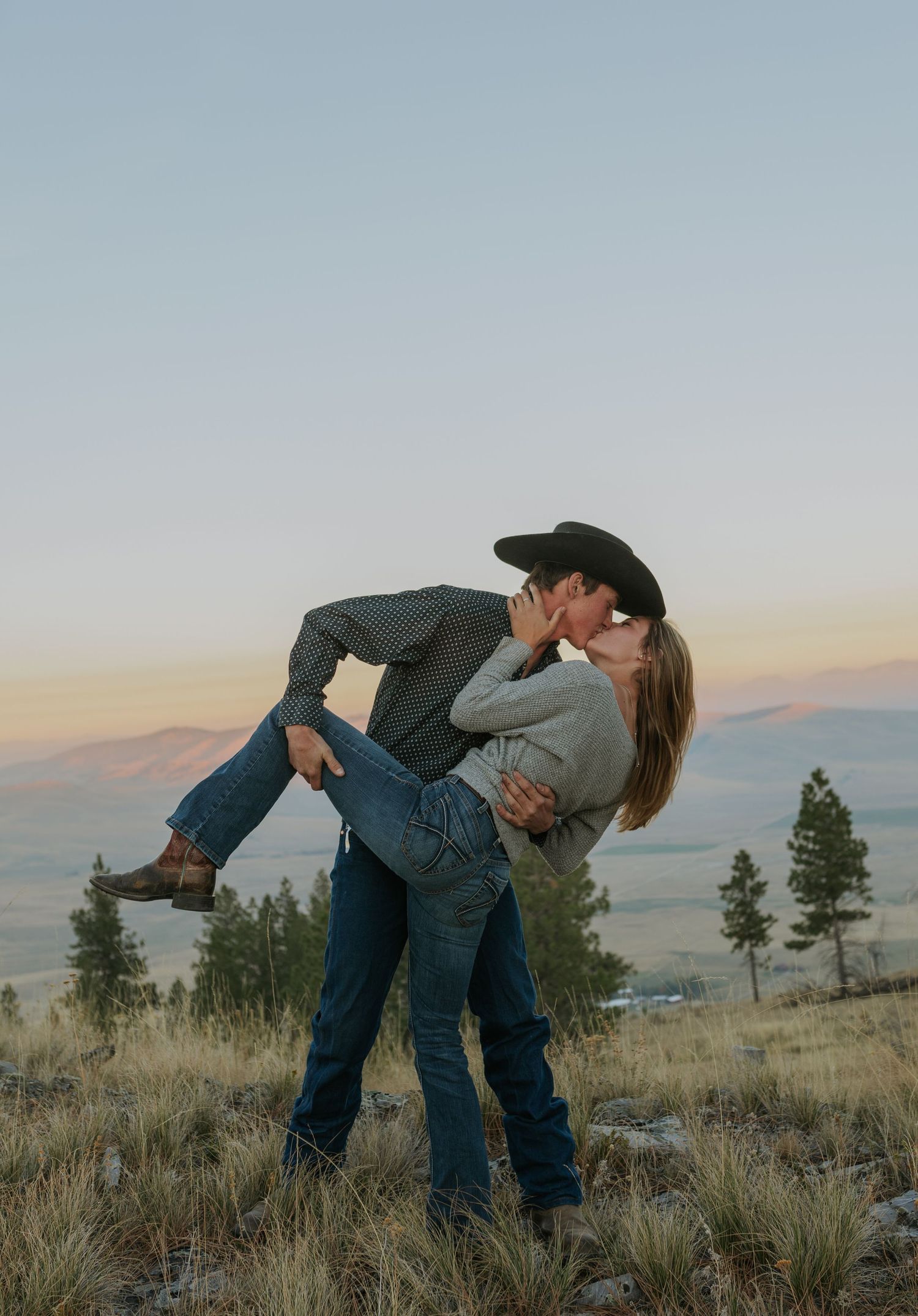 Dancing couple in western attire performs romantic dips against mountain landscape at sunset.