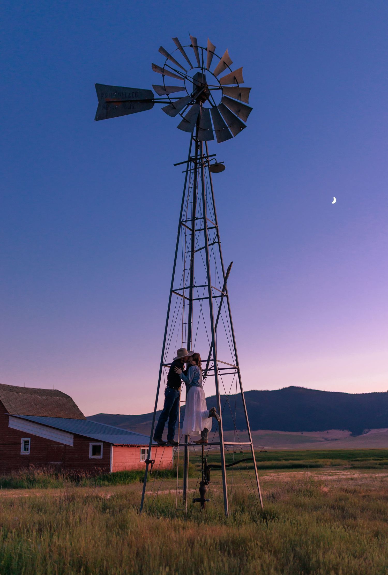 Silhouette of windmills against purple sunset sky with moon in rural landscape.