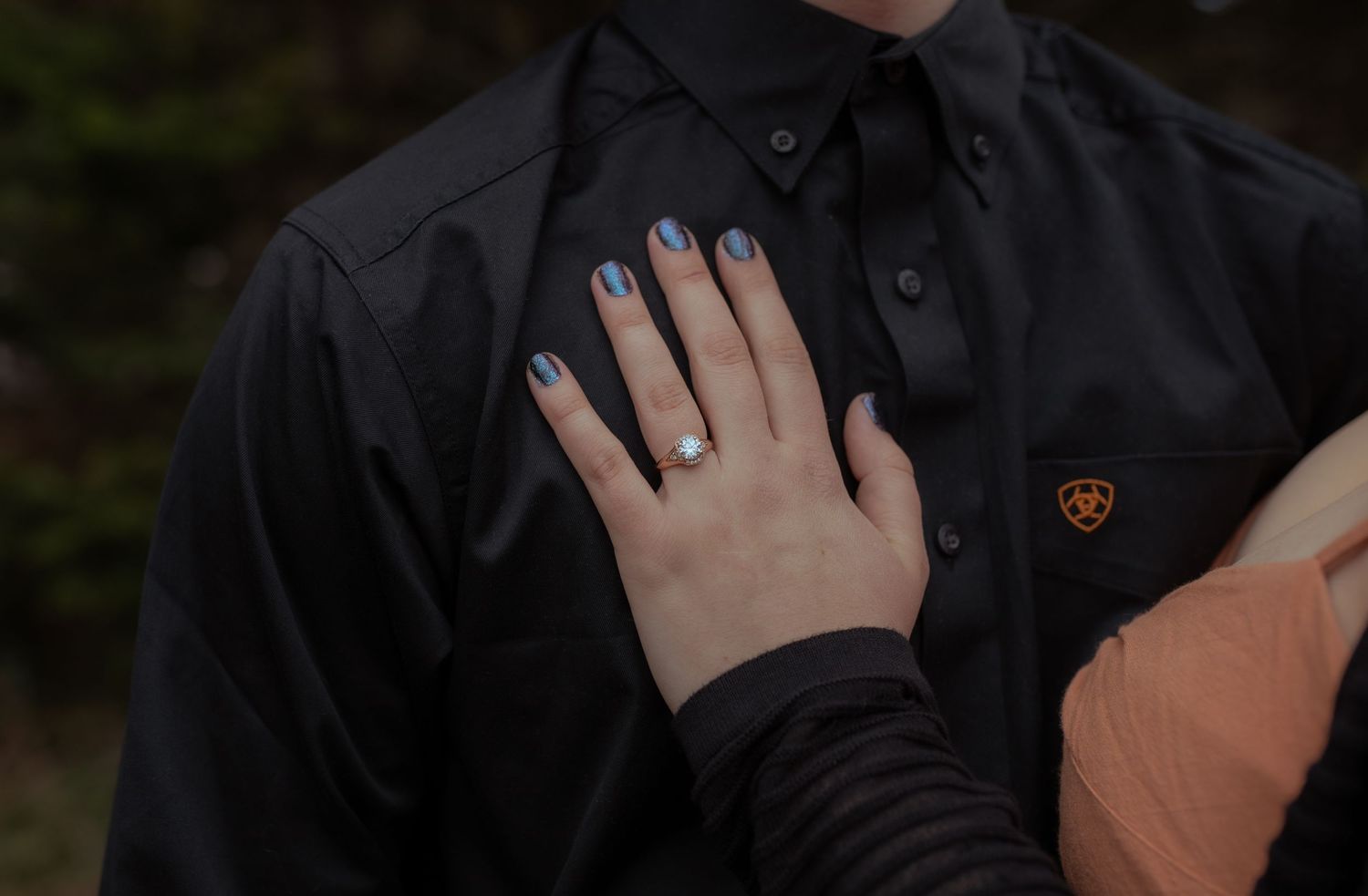 A close-up of hands with blue nail polish touching a black shirt with a small emblem.