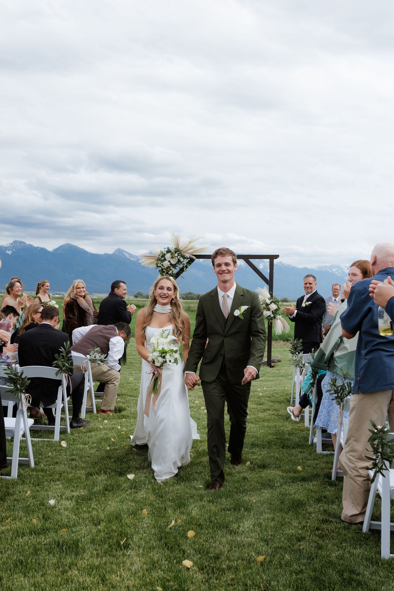 Bride and groom celebrate down outdoor aisle after wedding ceremony in Montana with mountain backdrop.