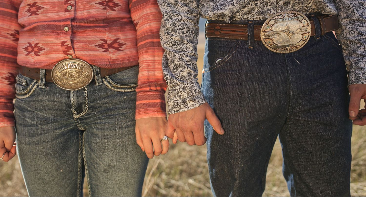 Close-up detail of western-style belt buckles and denim jeans.