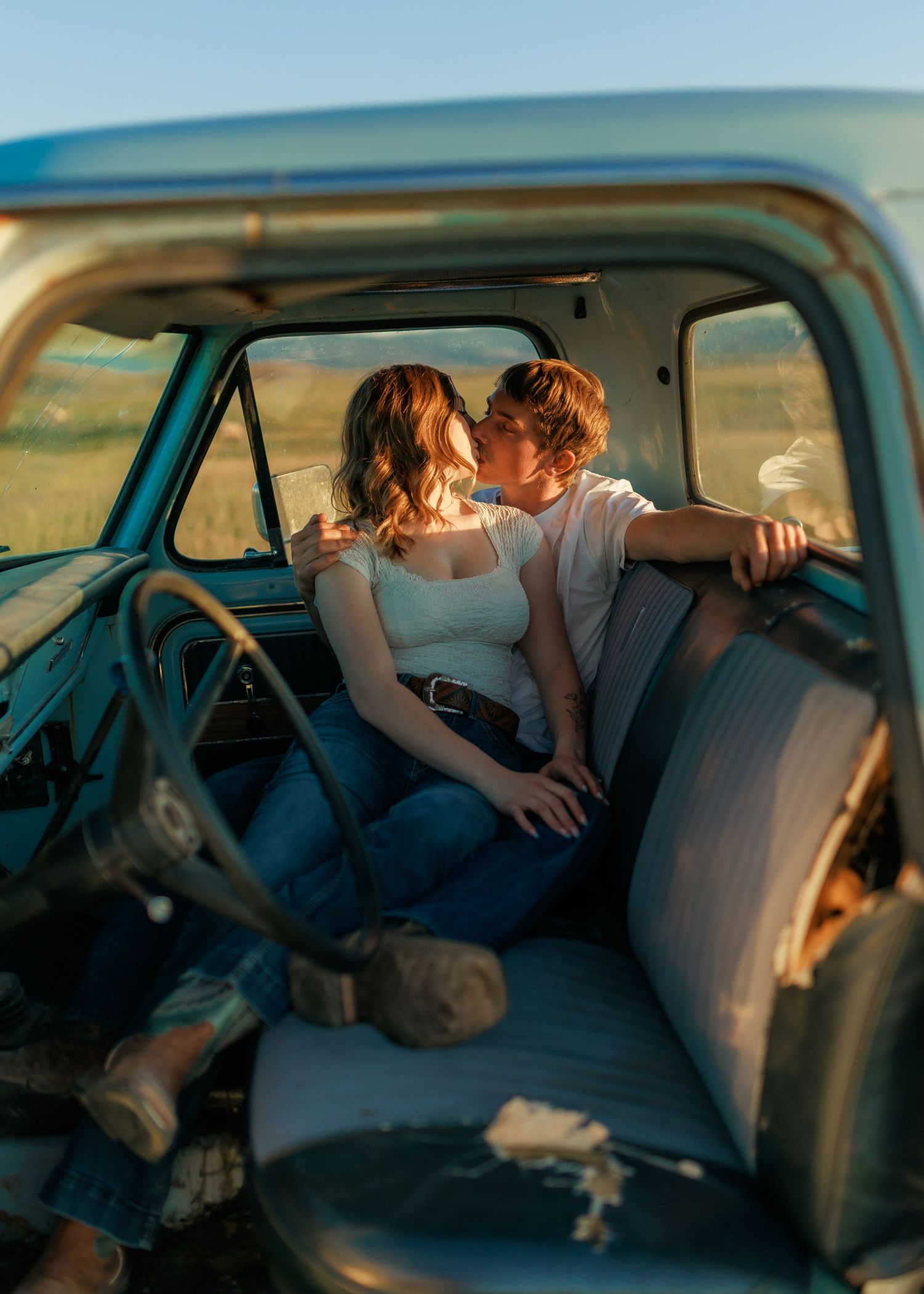 Tender moment captured inside vintage truck cab with sunset light streaming through windows.