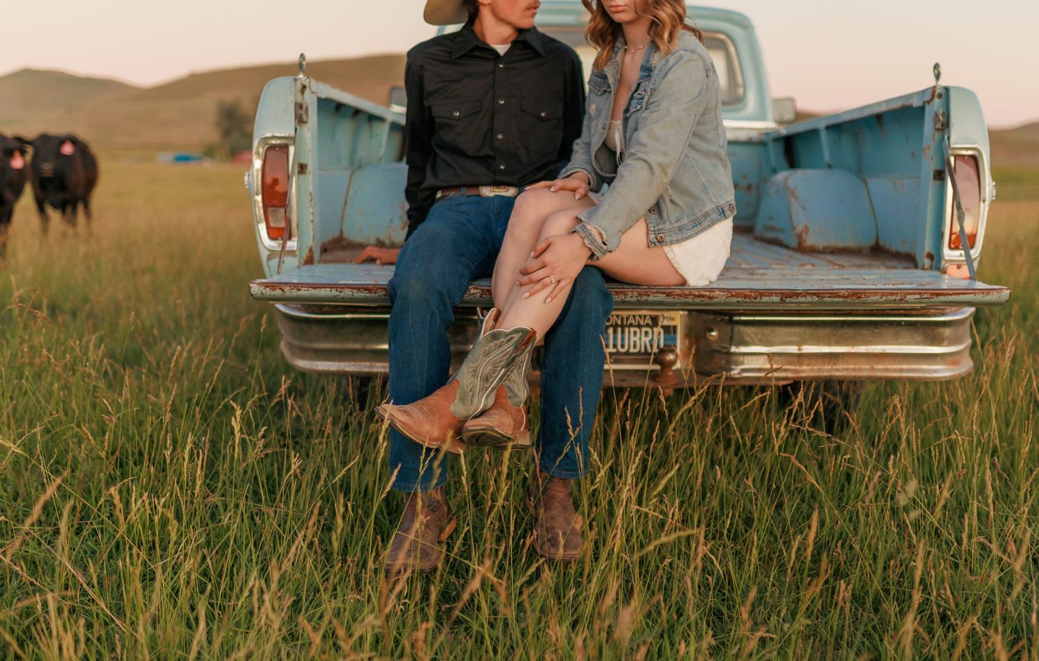 Couple relaxes on back of blue vintage pickup truck during sunset photo session.