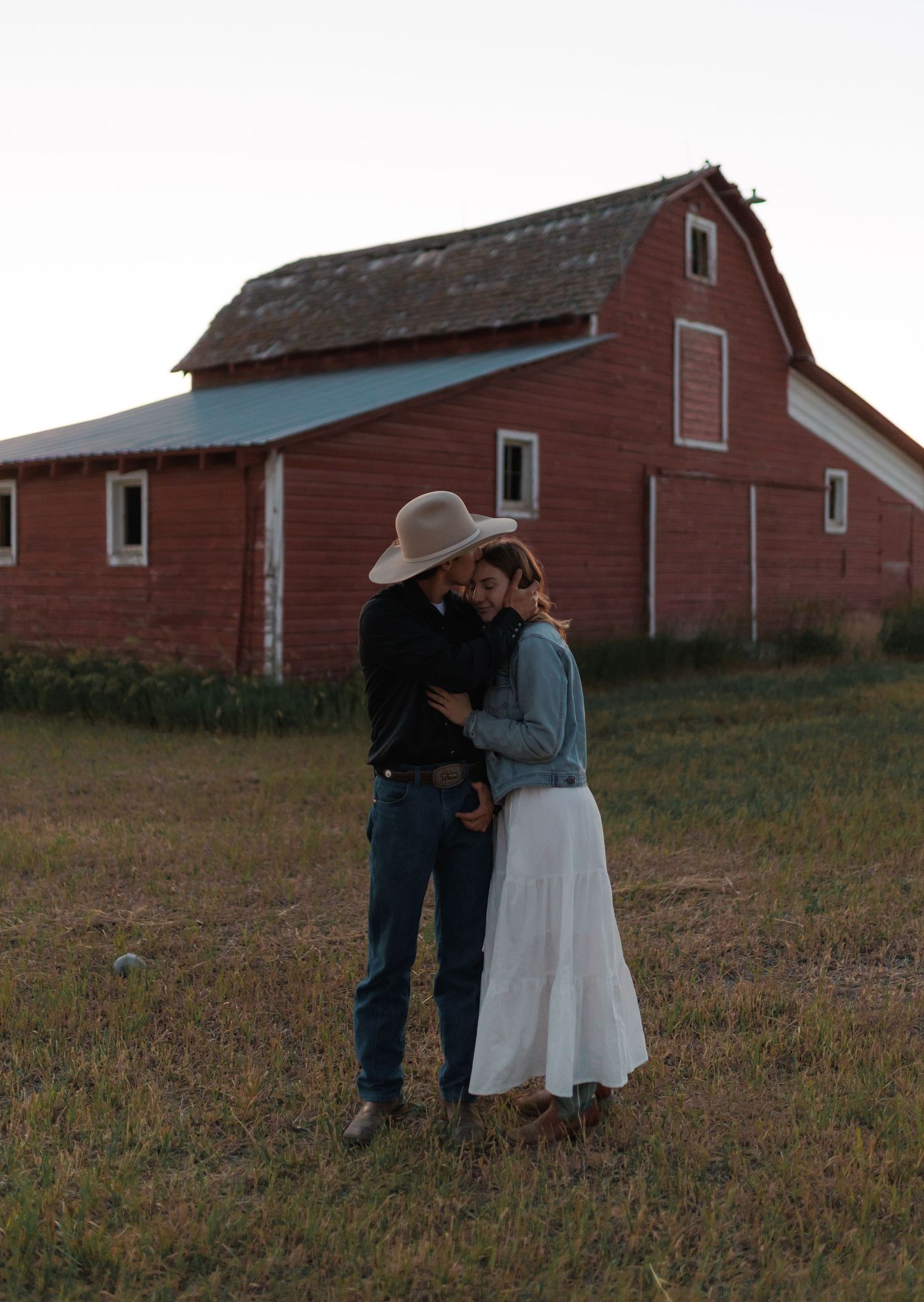 Rural engagement photos with vintage red barn backdrop at dusk.