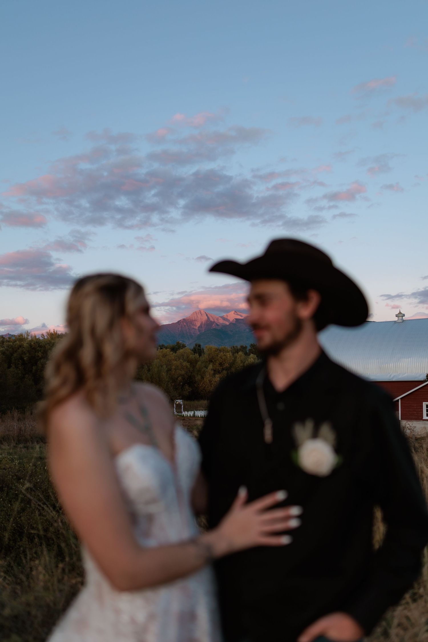 Couple in wedding attire at sunset with mountain alpenglow backdrop, groom in black cowboy hat and bride in lace dress in Montana.