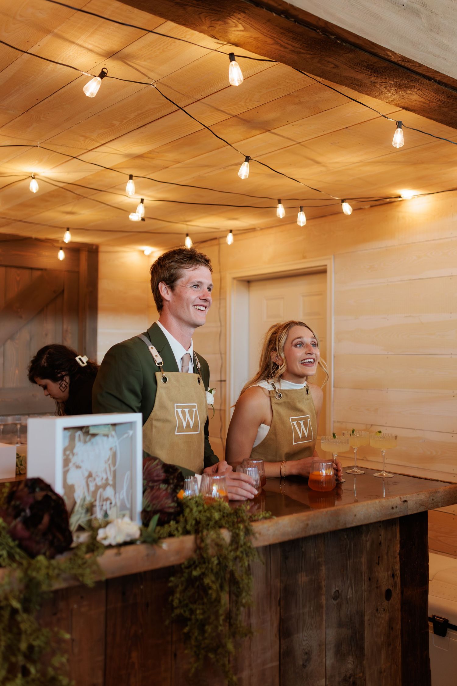 bride and groom bartending their cocktail hour with their signature drinks in matching aprons at Montana wedding