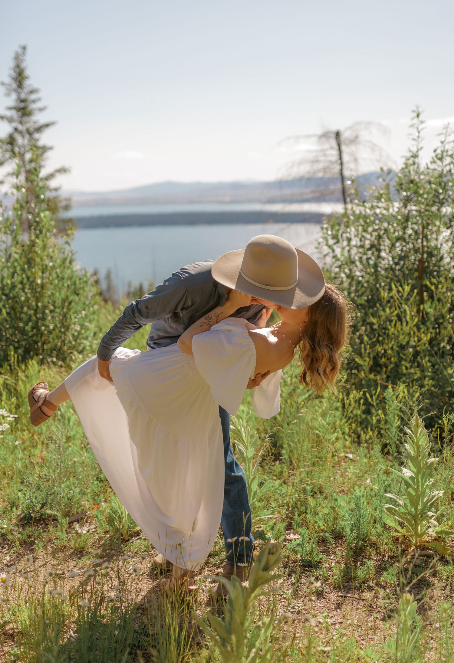 A romantic couple embraces in a wildflower field overlooking a lake on a sunny summer day.