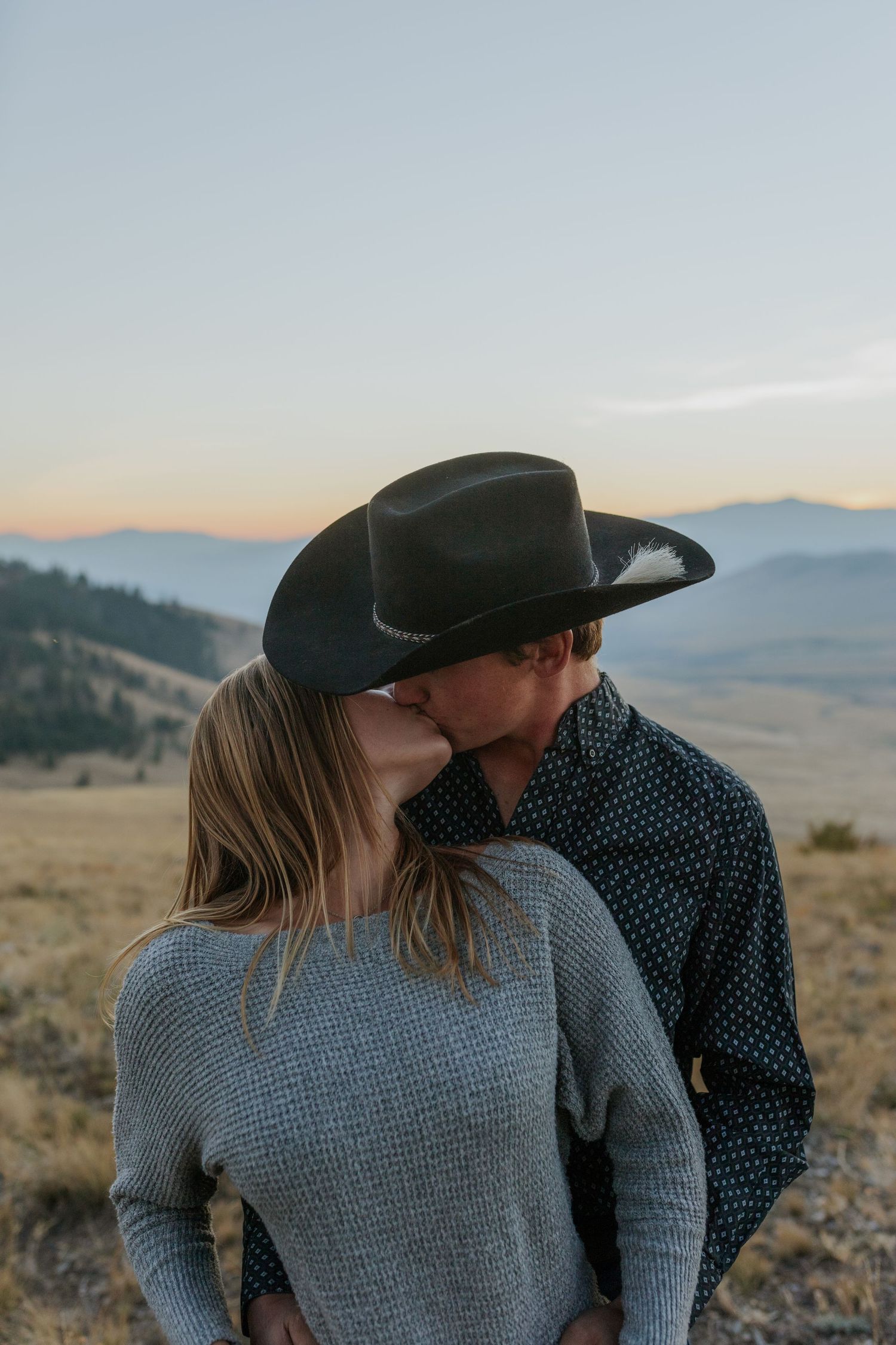 Couple in western and casual wear shares romantic moments against desert mountain landscape.
