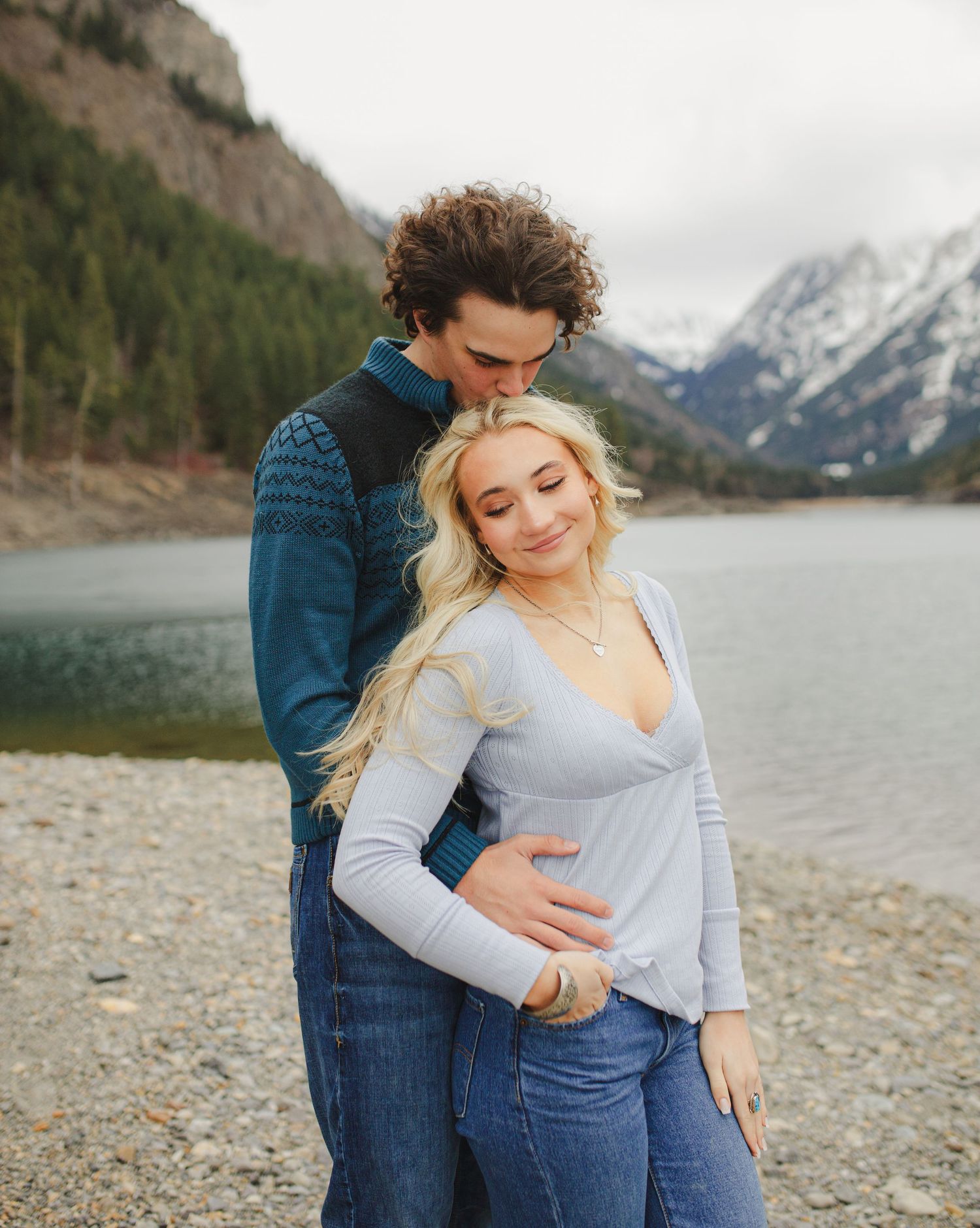 Tender moment between couple against backdrop of mountain lake and peaks.