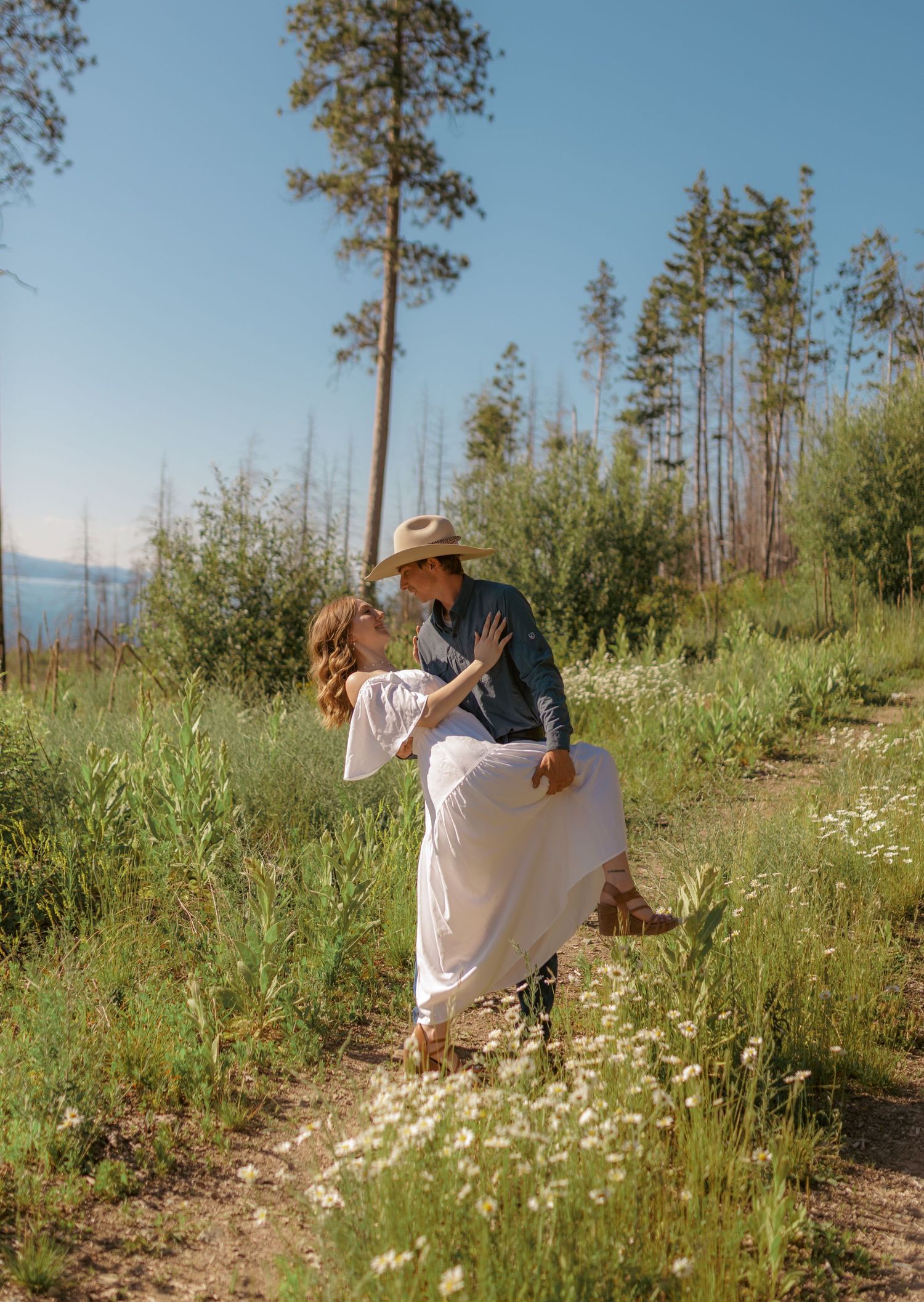 Couple dances together on a scenic mountain trail surrounded by wildflowers.