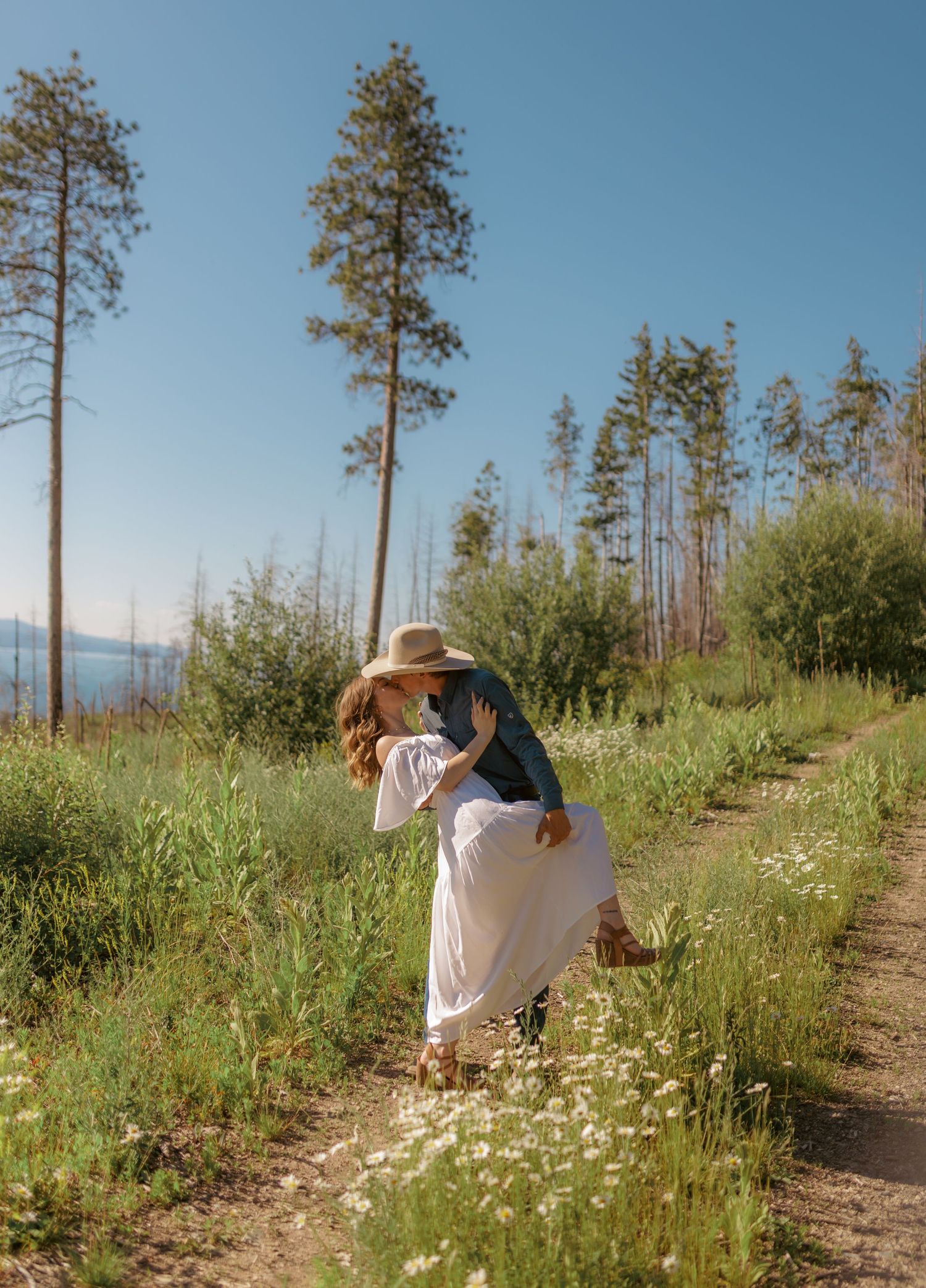 Romantic couple embraces among blooming daisies on a mountainside trail.