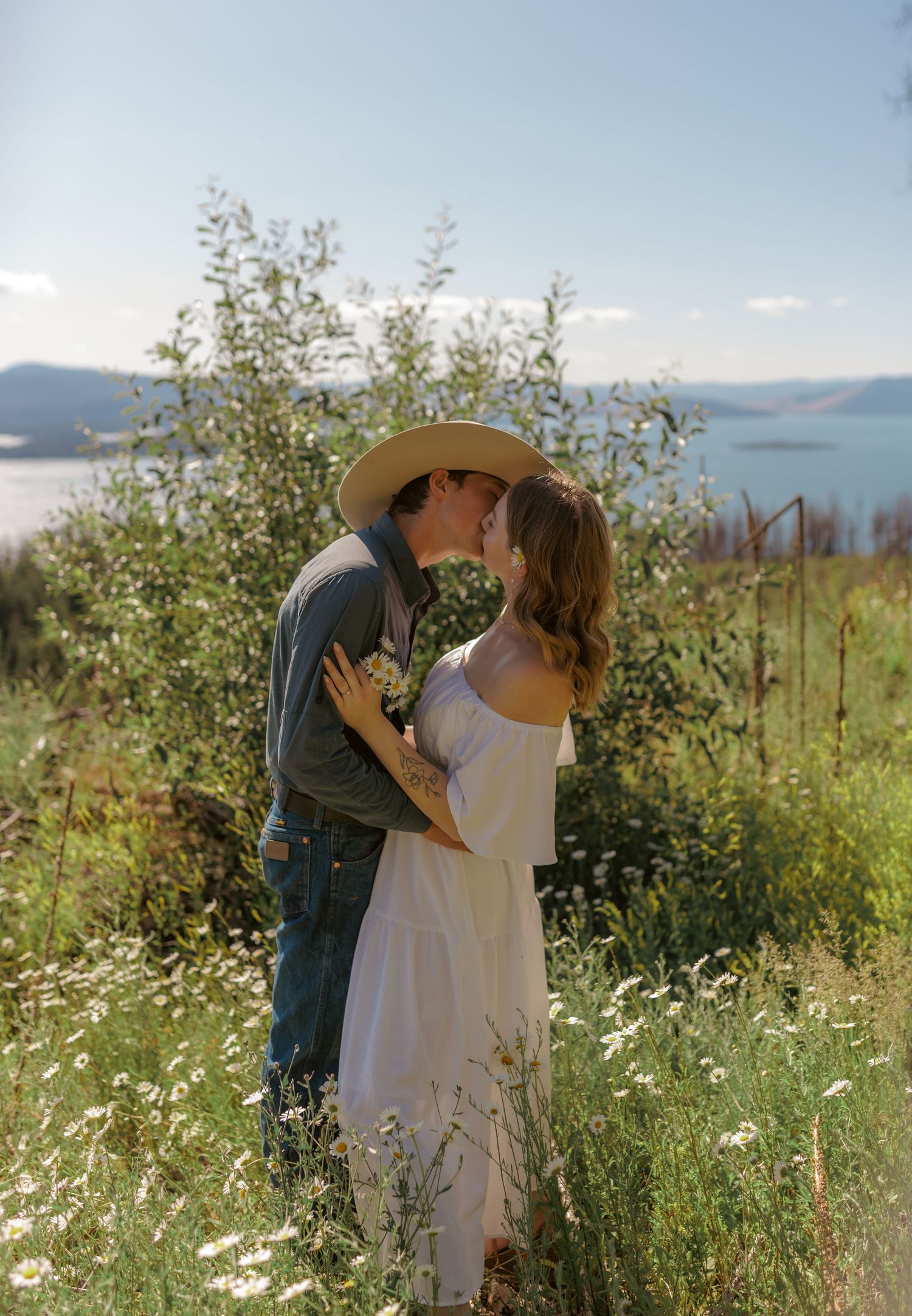A tender embrace in a sunny meadow filled with white daisies and mountain views.