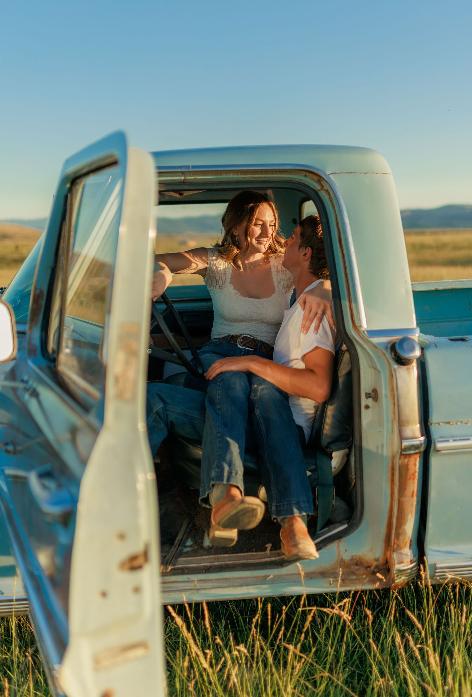 Joyful laughter shared inside vintage pickup truck against scenic landscape backdrop.