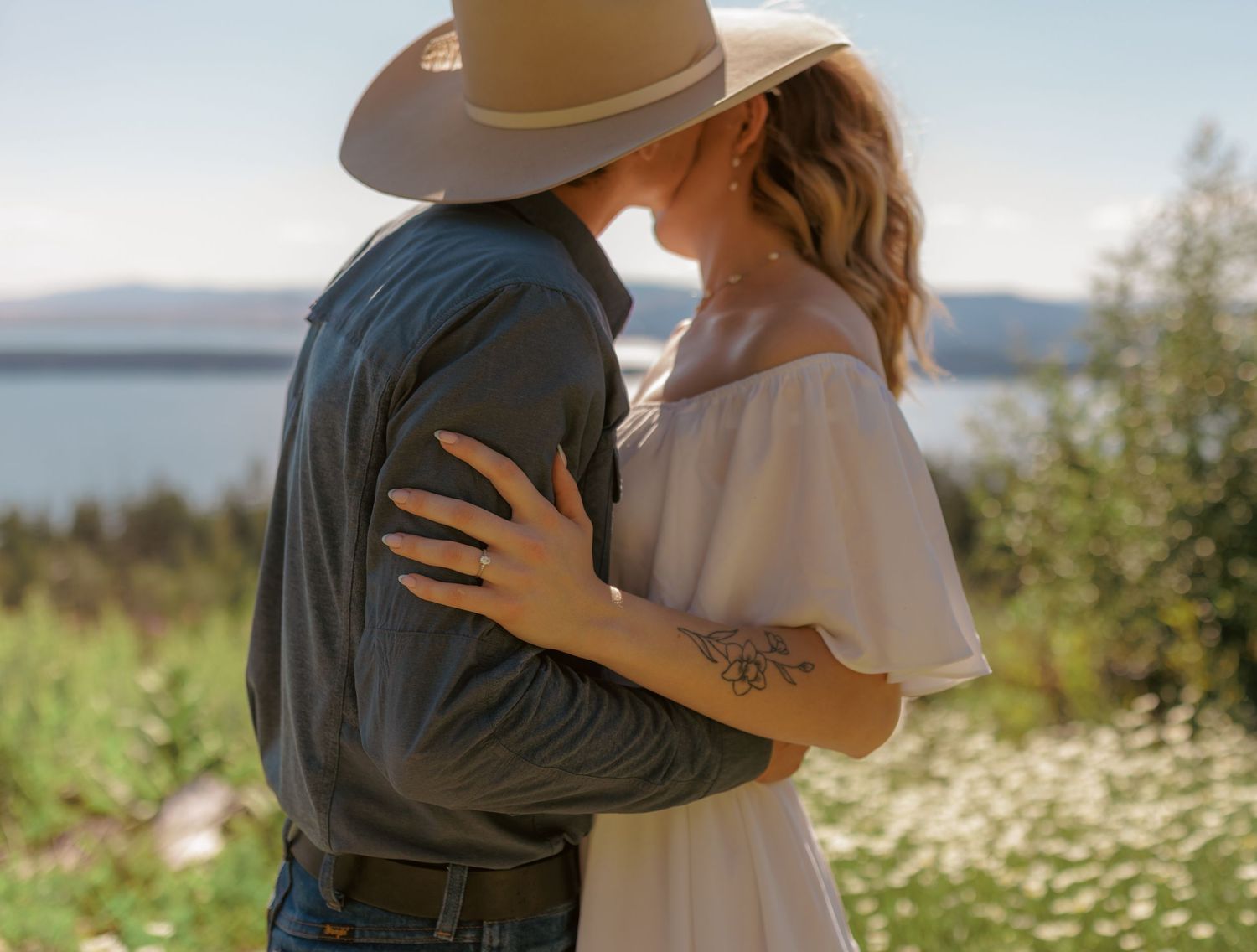 Two people share an intimate moment among wildflowers with scenic mountain views.