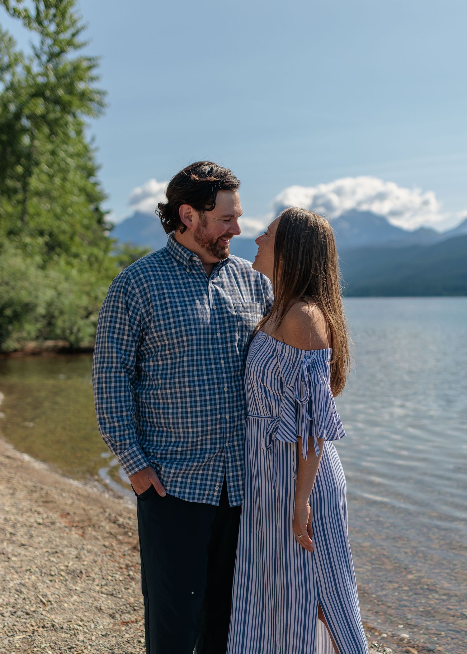 A couple shares an intimate moment by a lake with snow-capped mountains in the background.