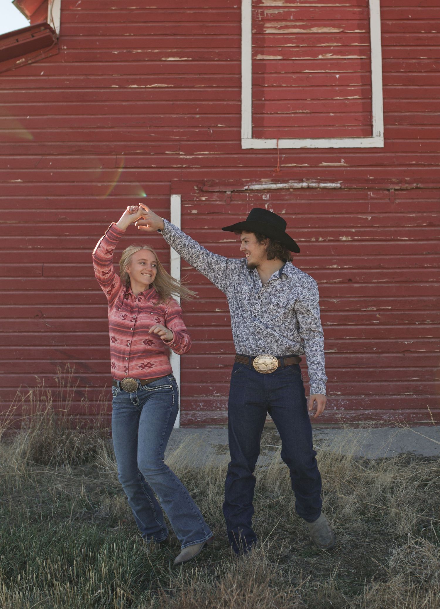 A couple dances together against the backdrop of a vintage red barn on a rural property.