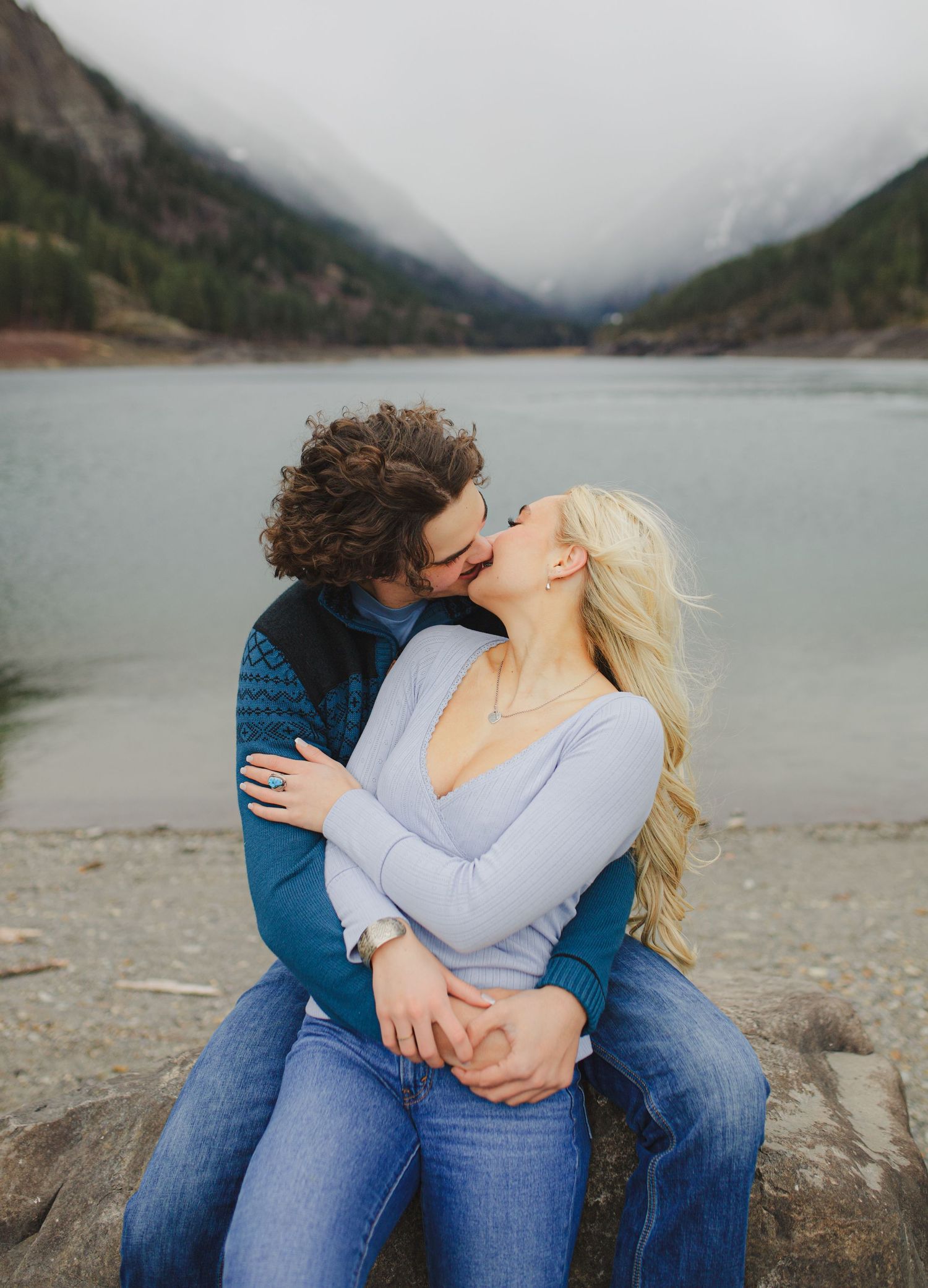 A couple shares an intimate moment on the shore of a misty mountain lake.