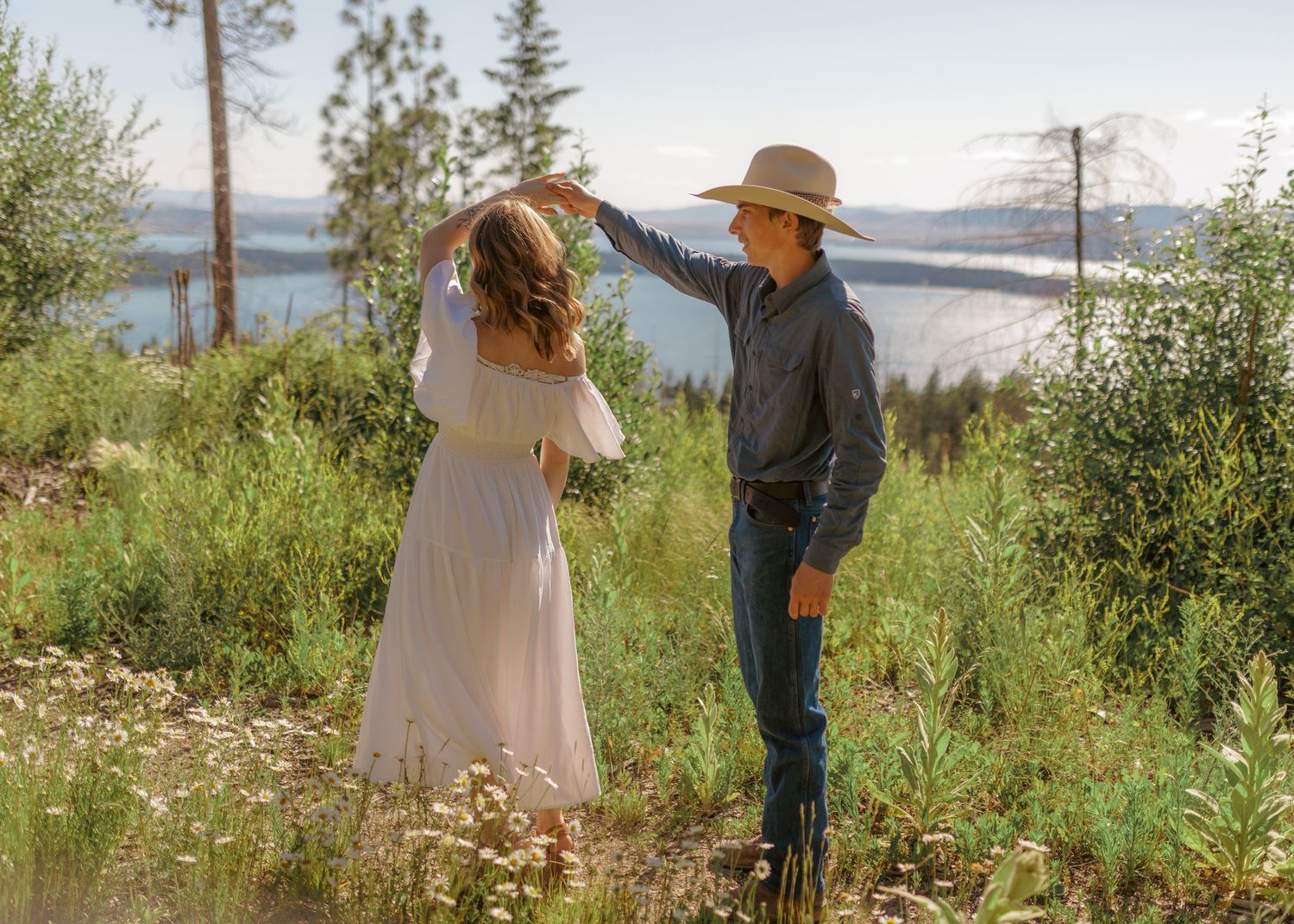 Wide landscape shot of a couple's romantic moments in a mountain meadow.