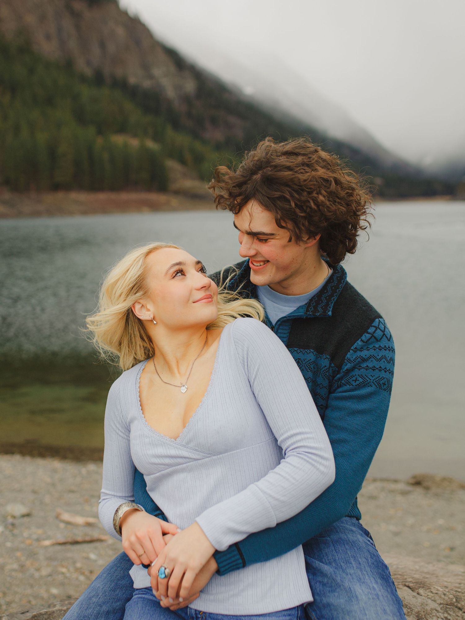 A romantic couple embraces by a mountain lake on a moody afternoon.
