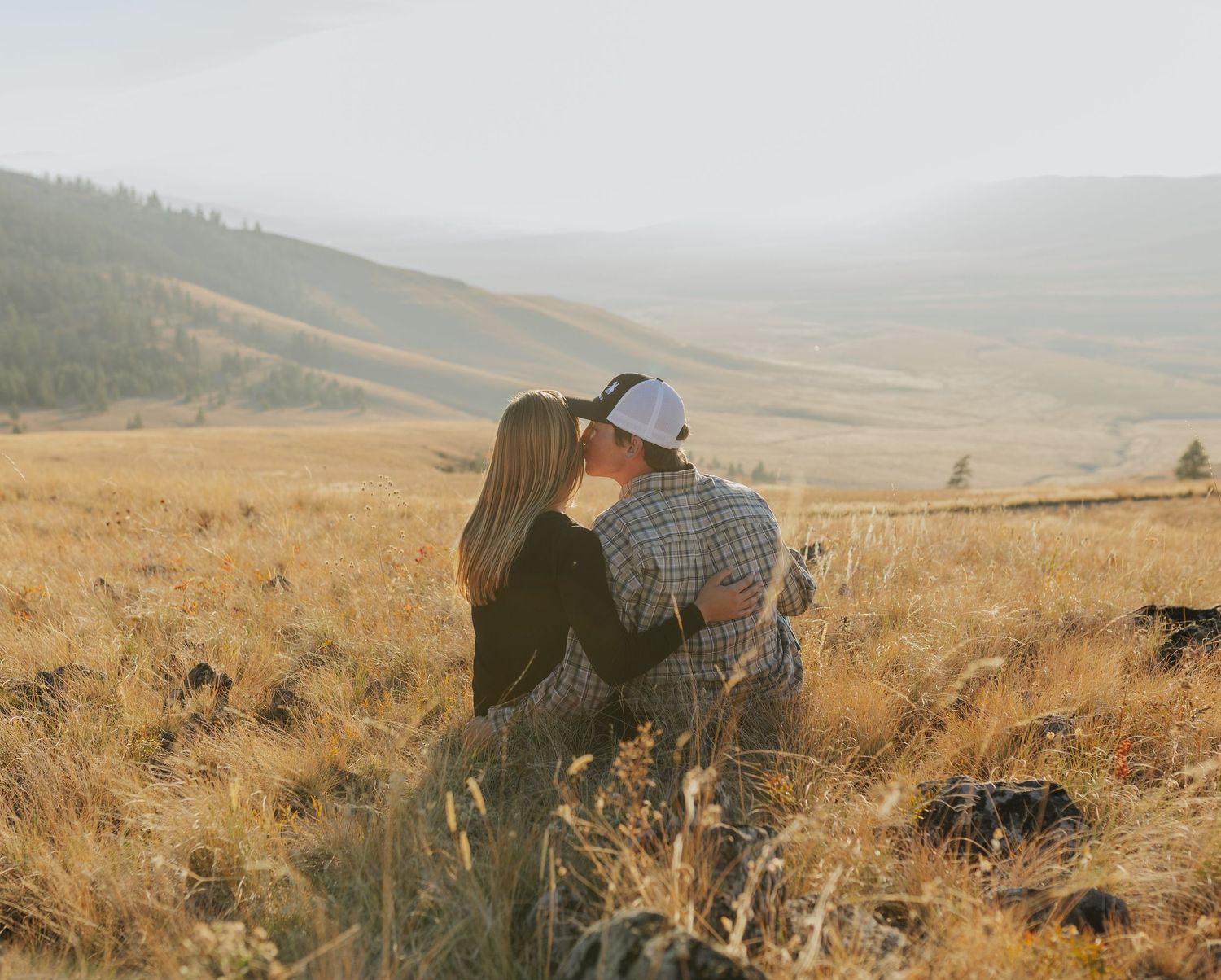 A couple embraces while overlooking rolling hills at sunset.