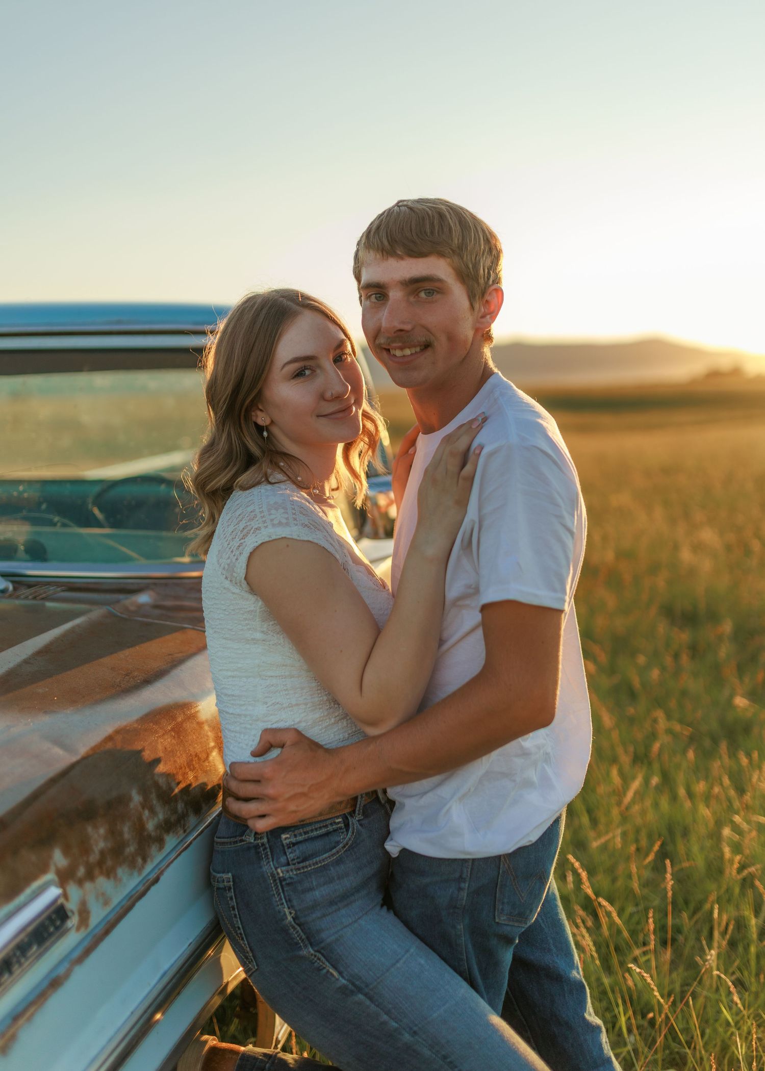 Intimate embrace near classic truck in rural field during golden hour sunset.