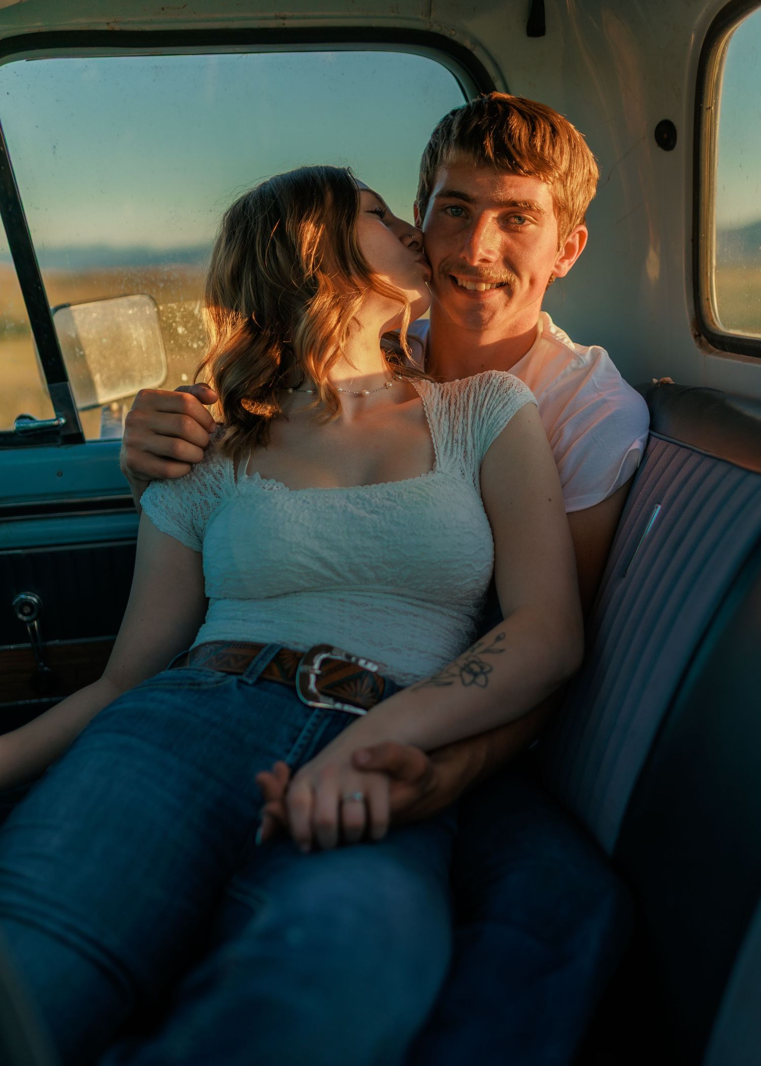Couple sharing intimate moment in vintage truck during golden hour sunset.