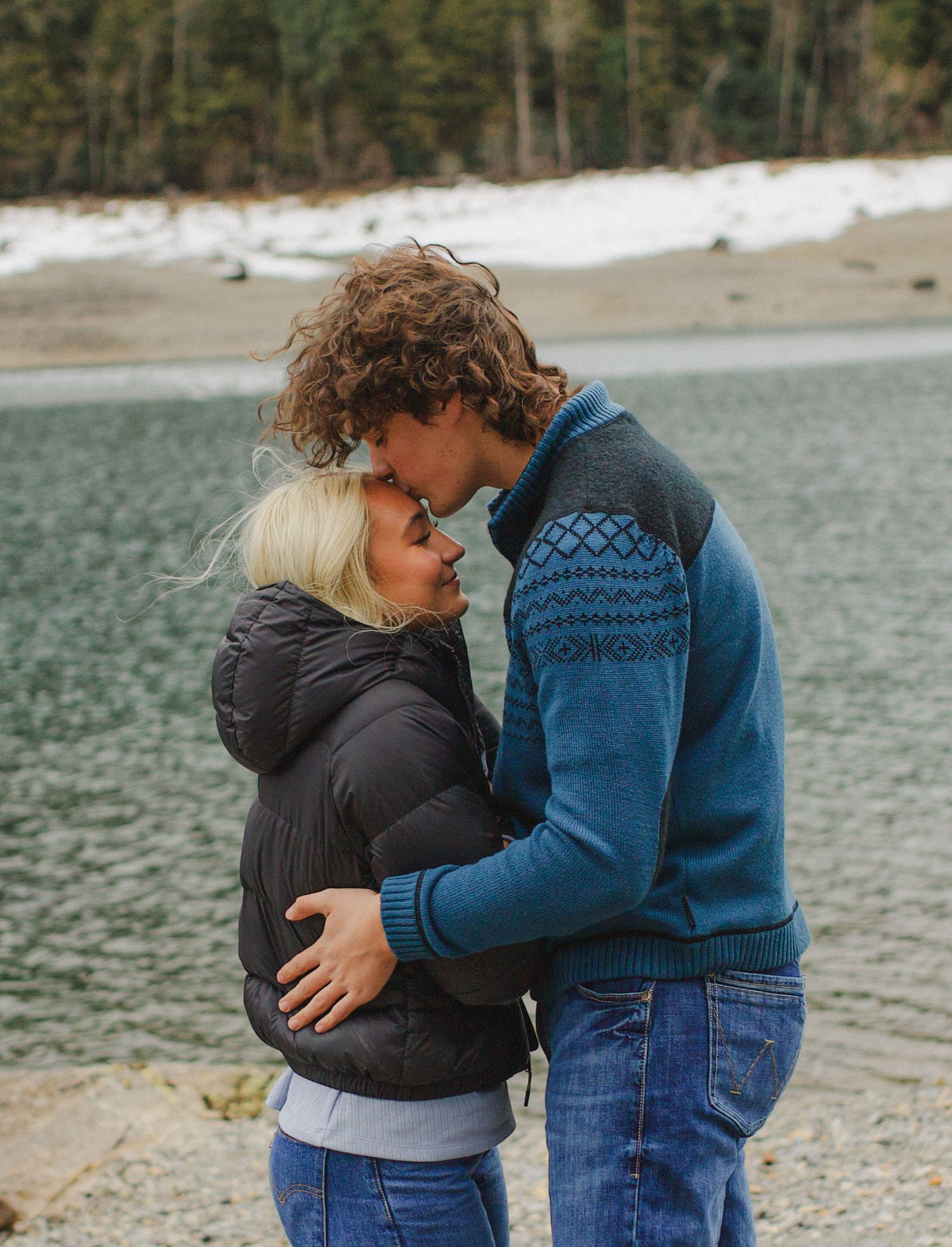 Intimate moment between couple on a rocky beach with mountains in background.