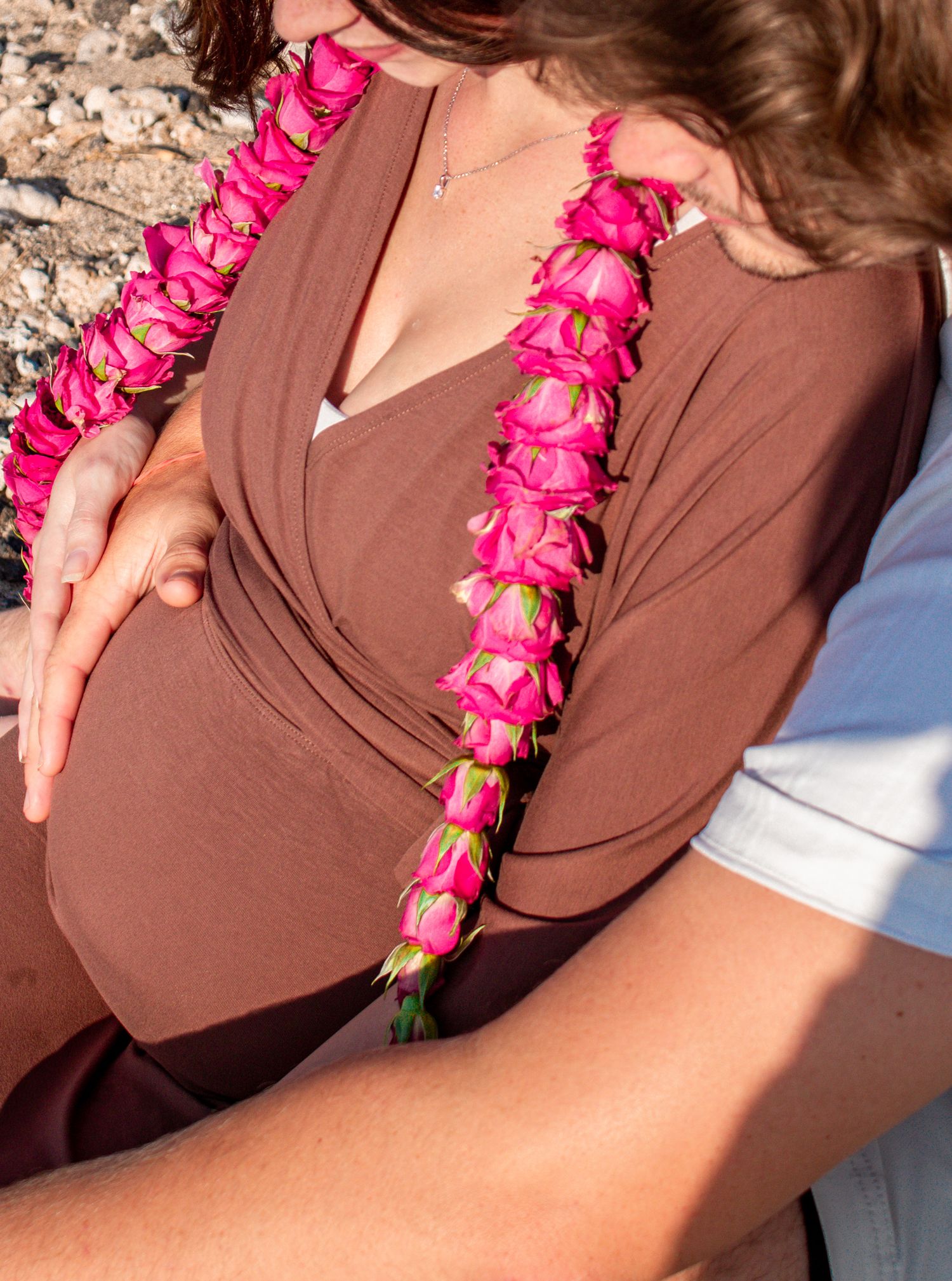 A bright pink flower lei draped over a brown dress creates a vibrant tropical accent against the fabric.